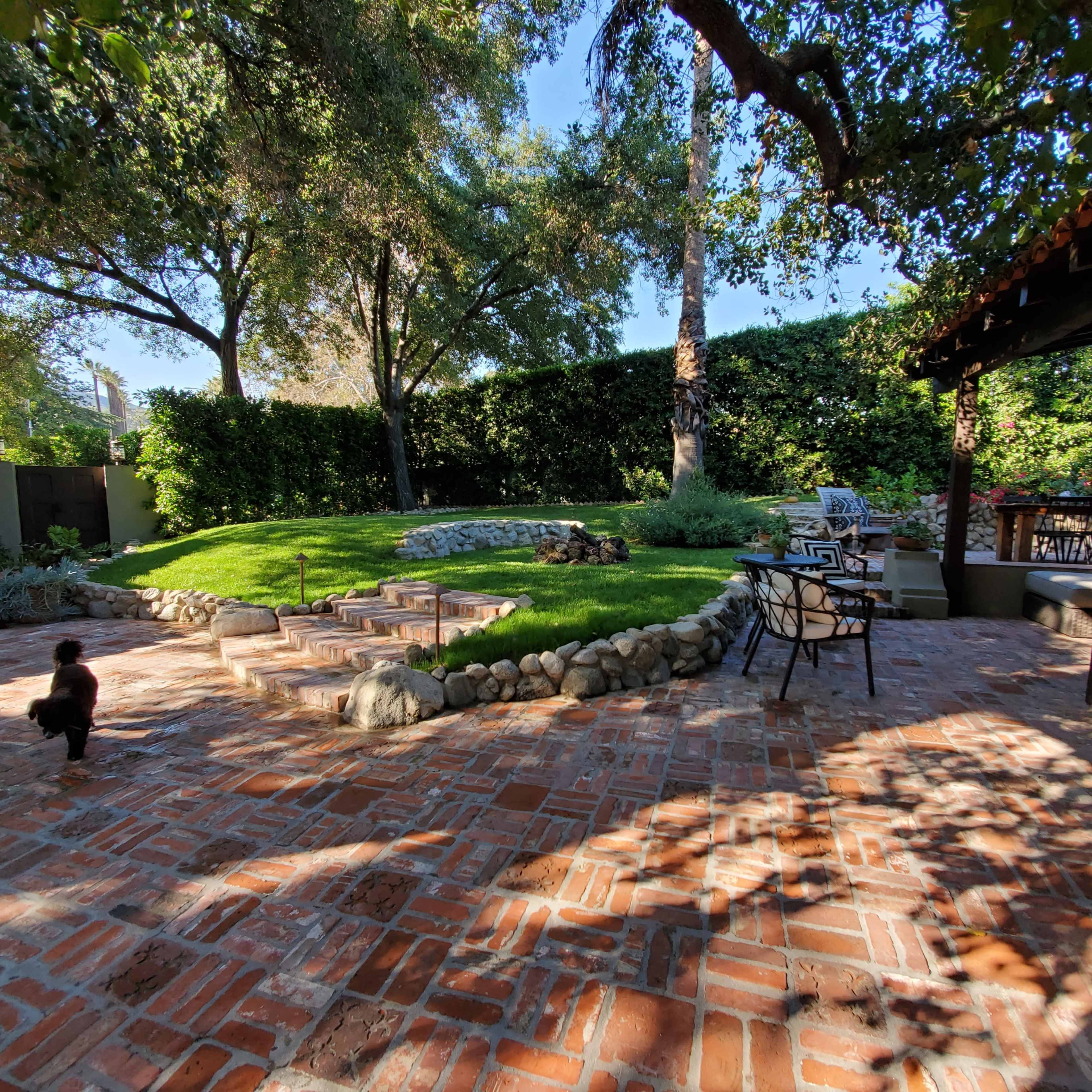 A landscaped backyard with a stone pathway, grass area, and seating arrangements under a shaded patio.
