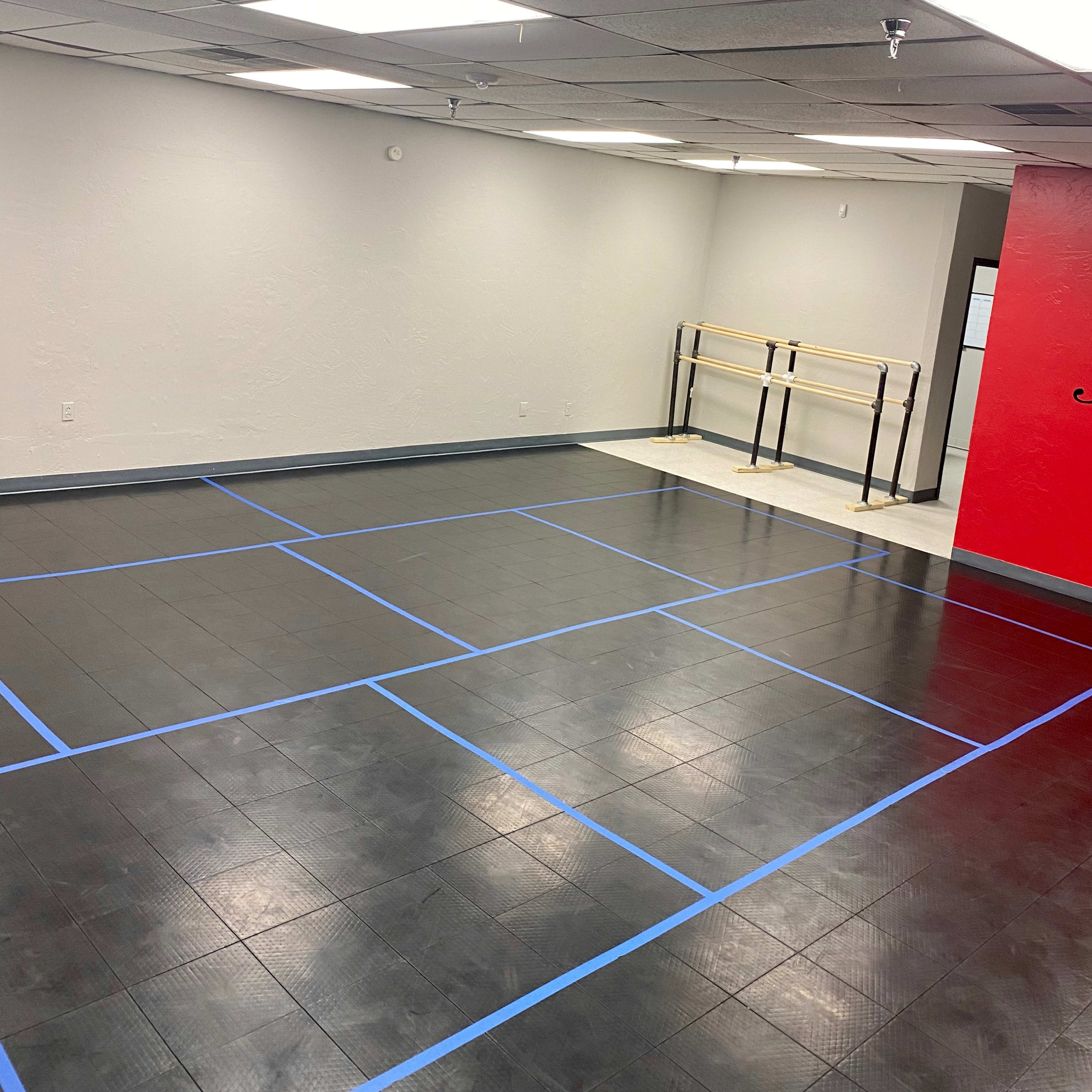 A spacious empty room with blue tape marking a dance floor layout and a red wall on one side.