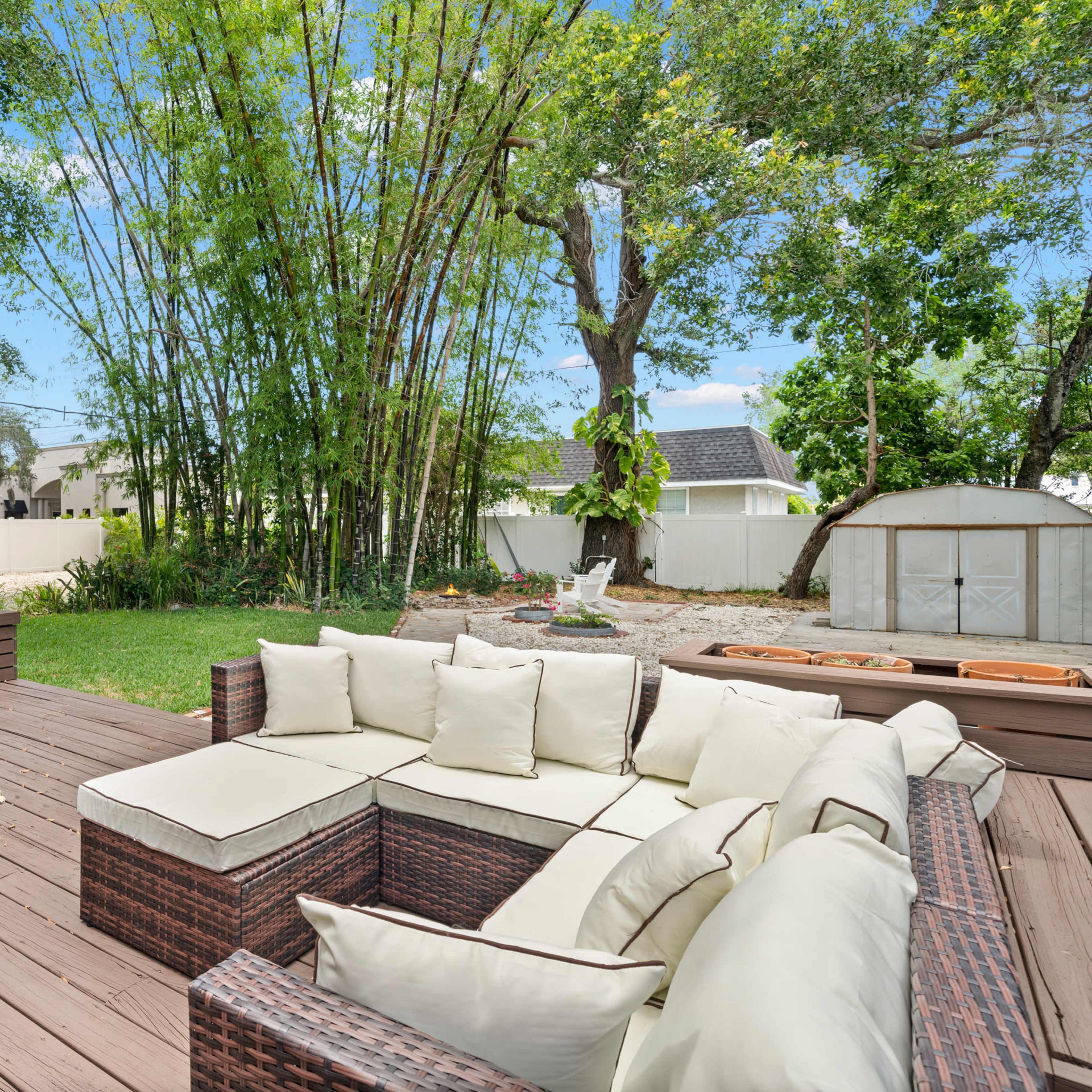 A wooden deck with a sectional outdoor sofa and a backdrop of bamboo and trees in a backyard setting.