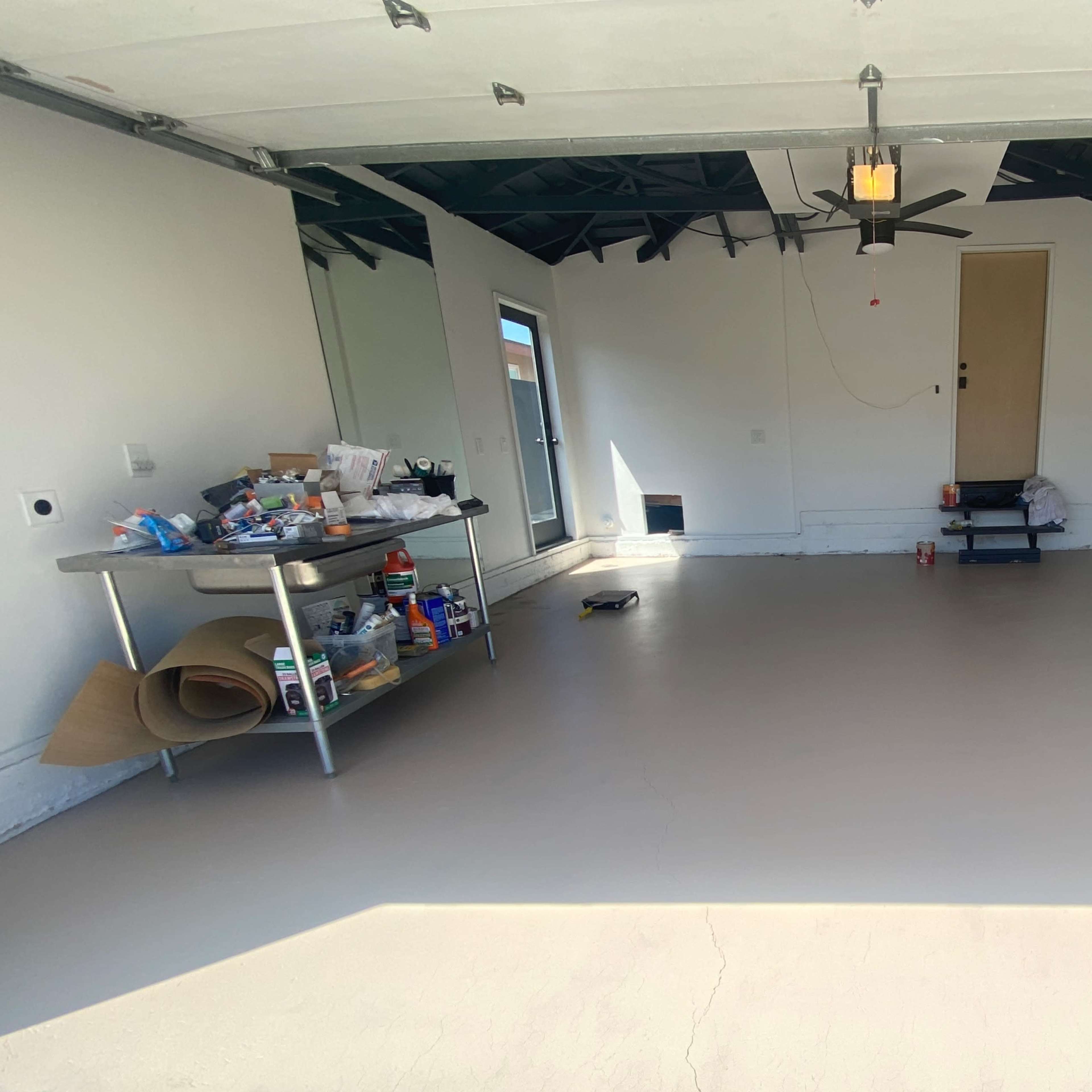 A clean, empty garage space with a table on one side filled with various tools and supplies, and a door leading outside.