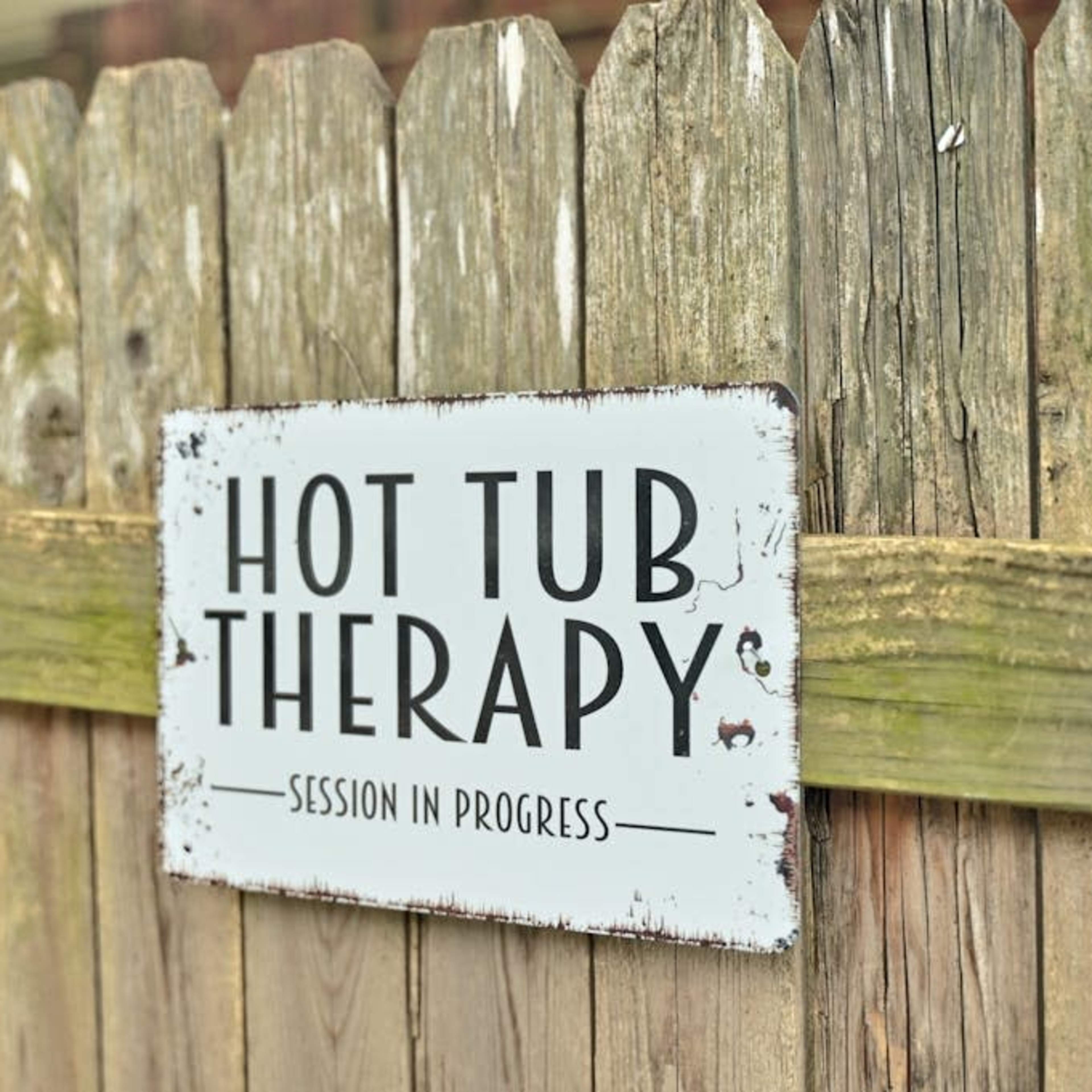 A weathered wooden fence displays a sign that reads "HOT TUB THERAPY" with the phrase "SESSION IN PROGRESS."