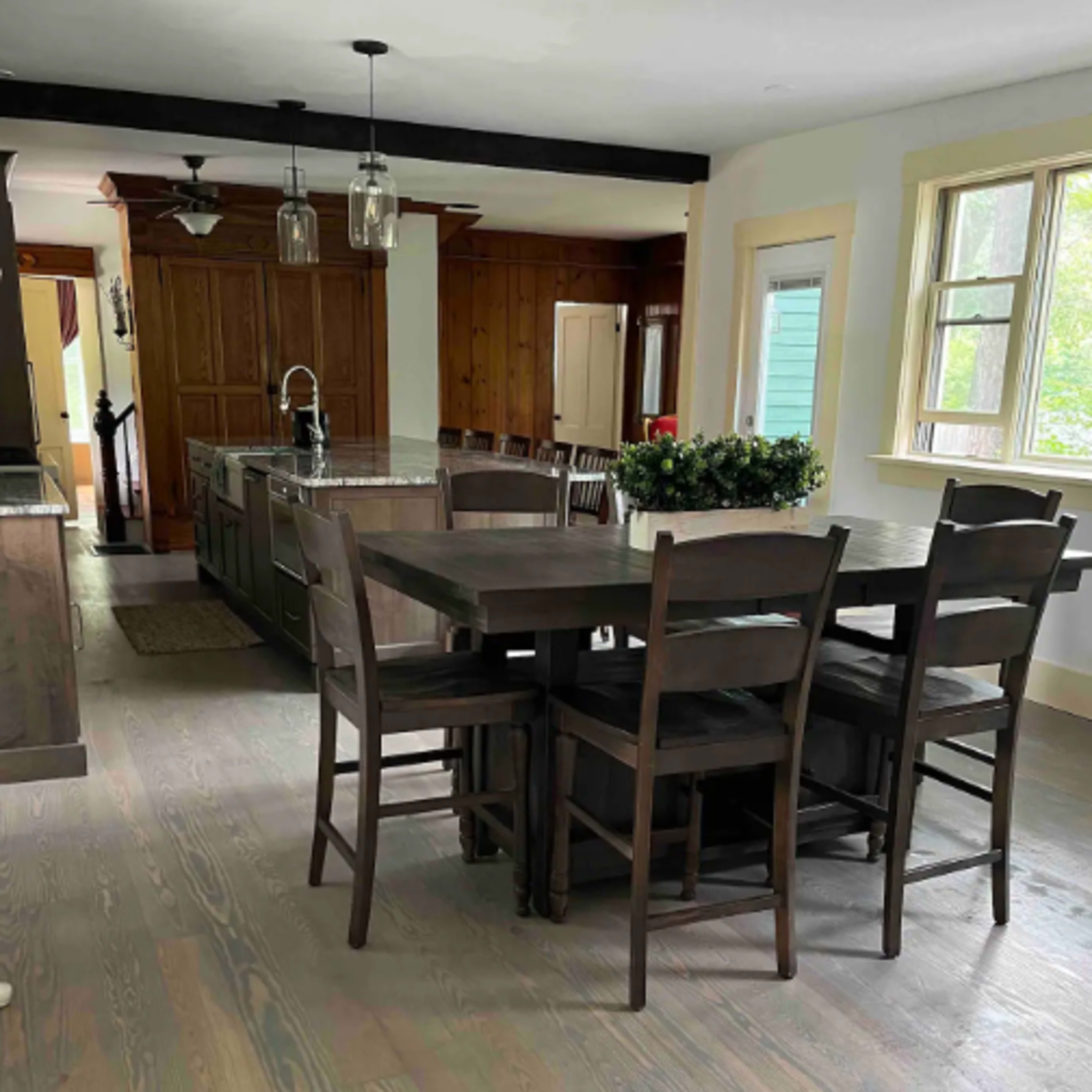 A spacious kitchen area featuring a large dining table with chairs, an island with a sink, and wooden cabinetry in the background.