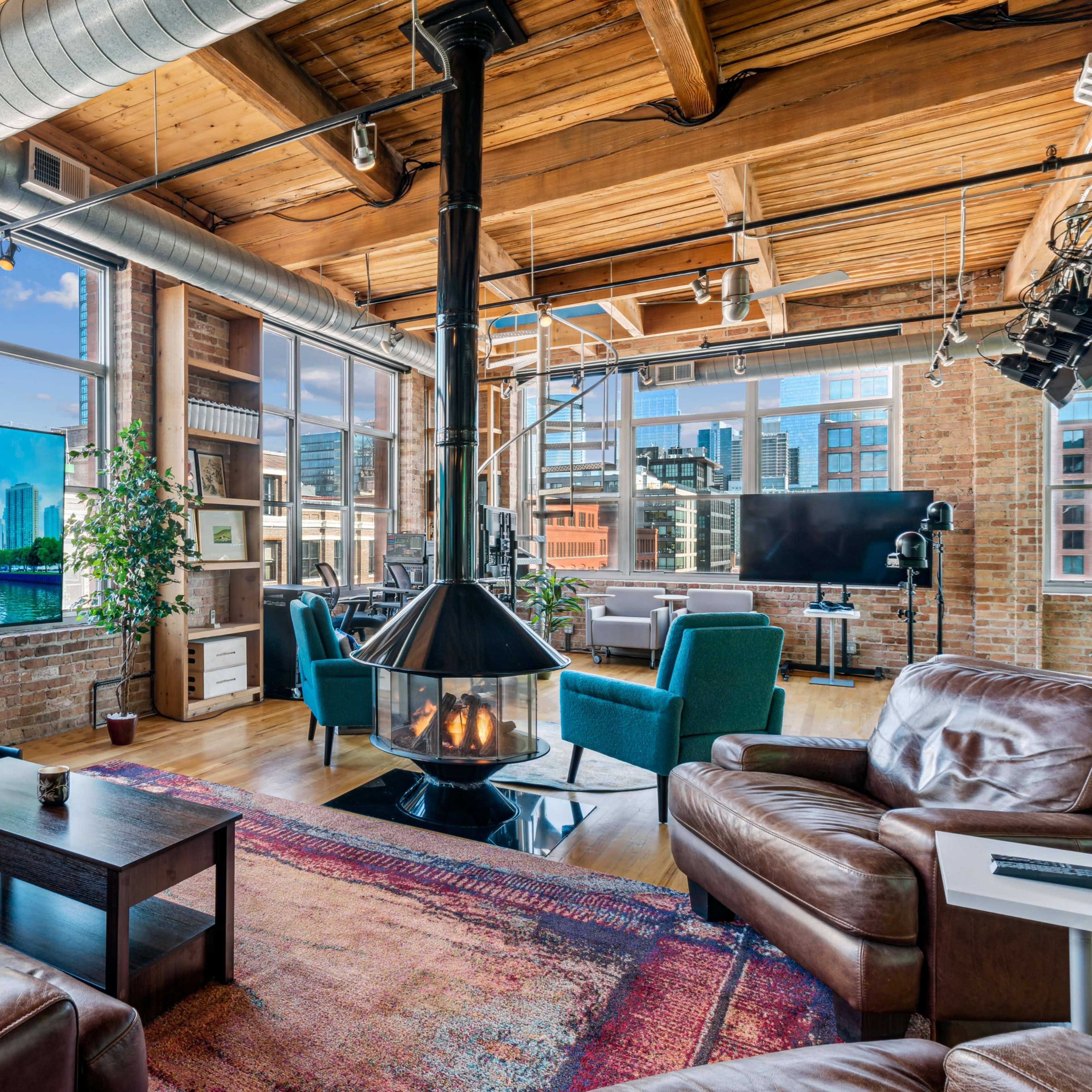 A spacious loft-style living area with large windows, a modern television, a central fireplace, and comfortable seating arrangements.