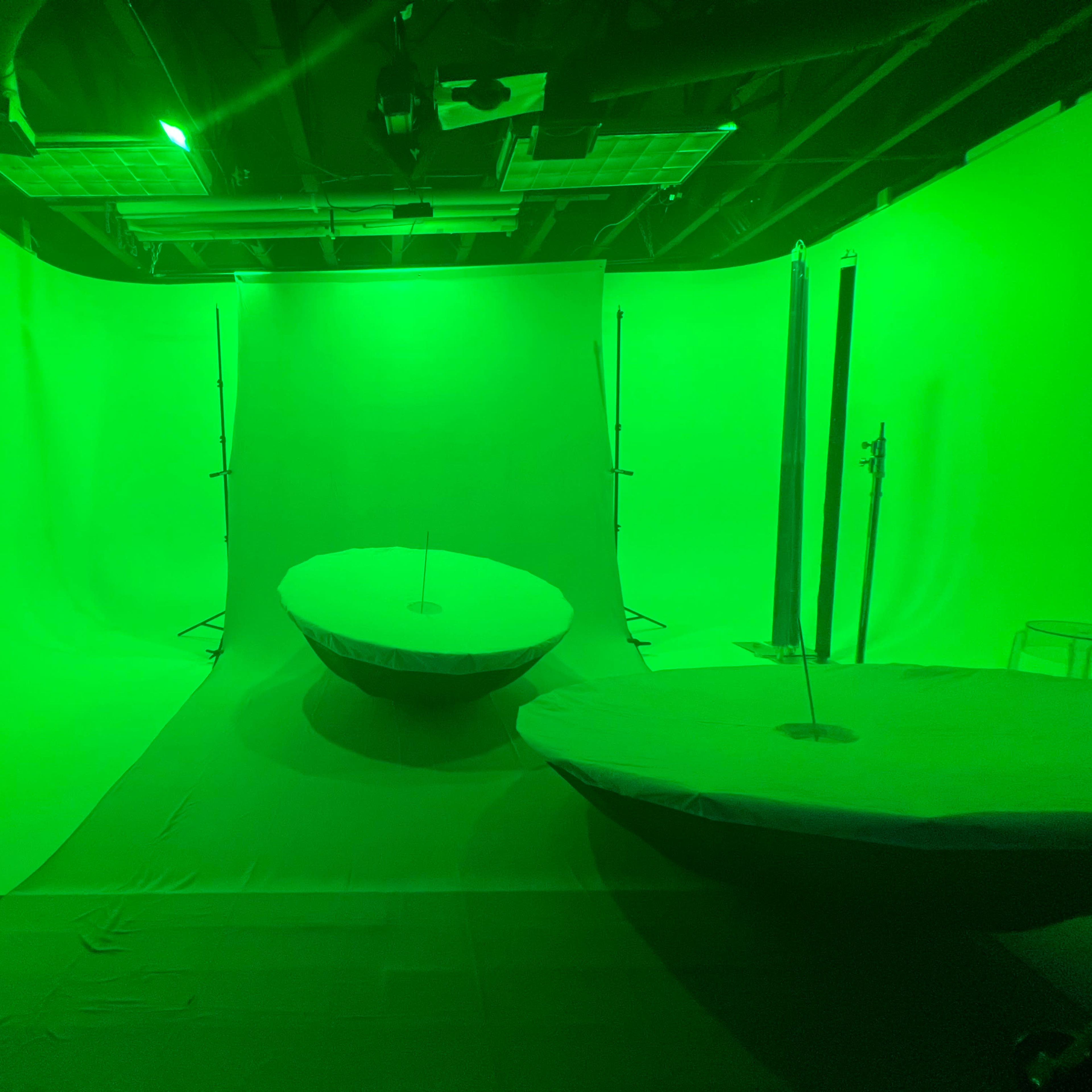 A green-lit studio with two circular tables in a space surrounded by green backdrops.