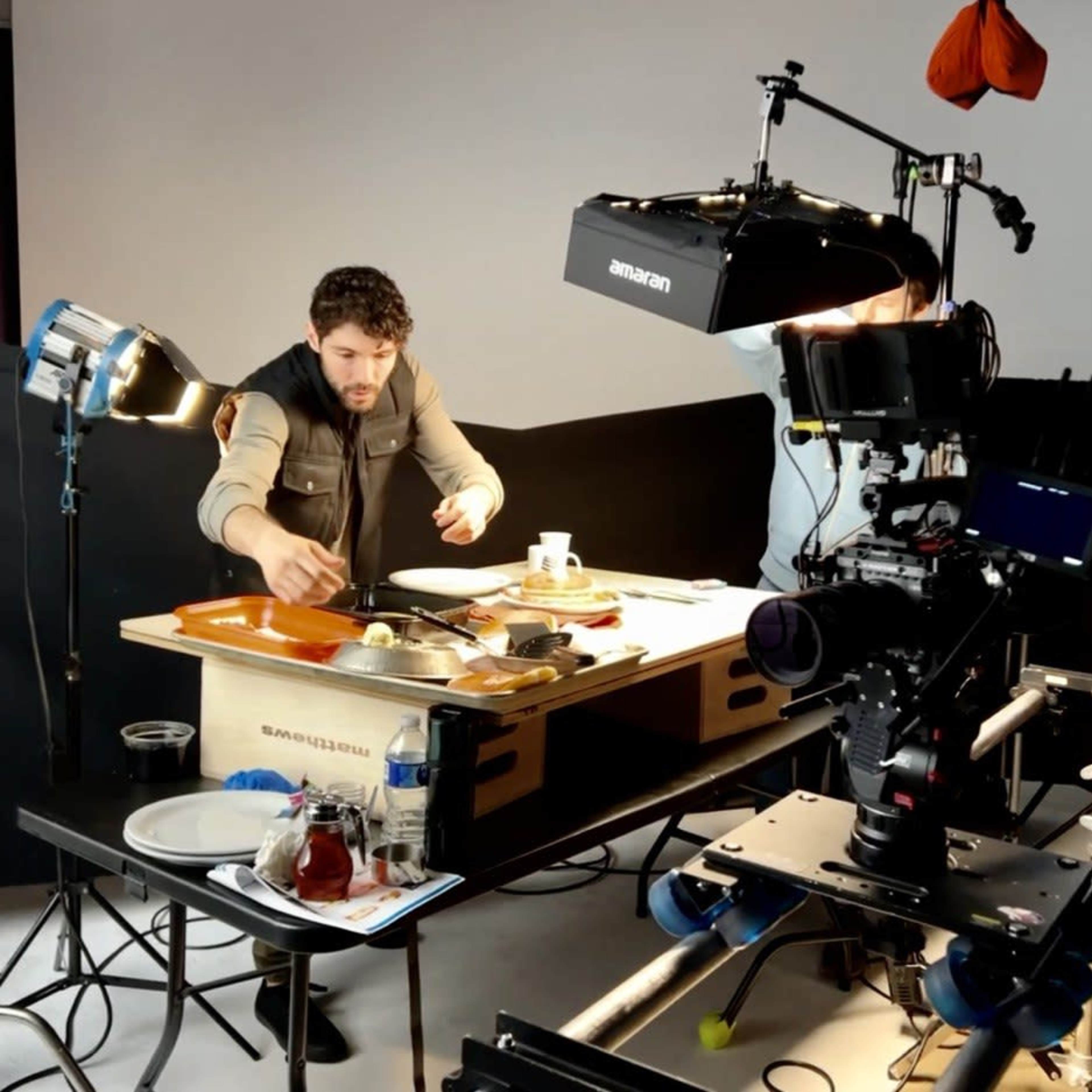 A man prepares food at a photography studio equipped with lights and cameras.