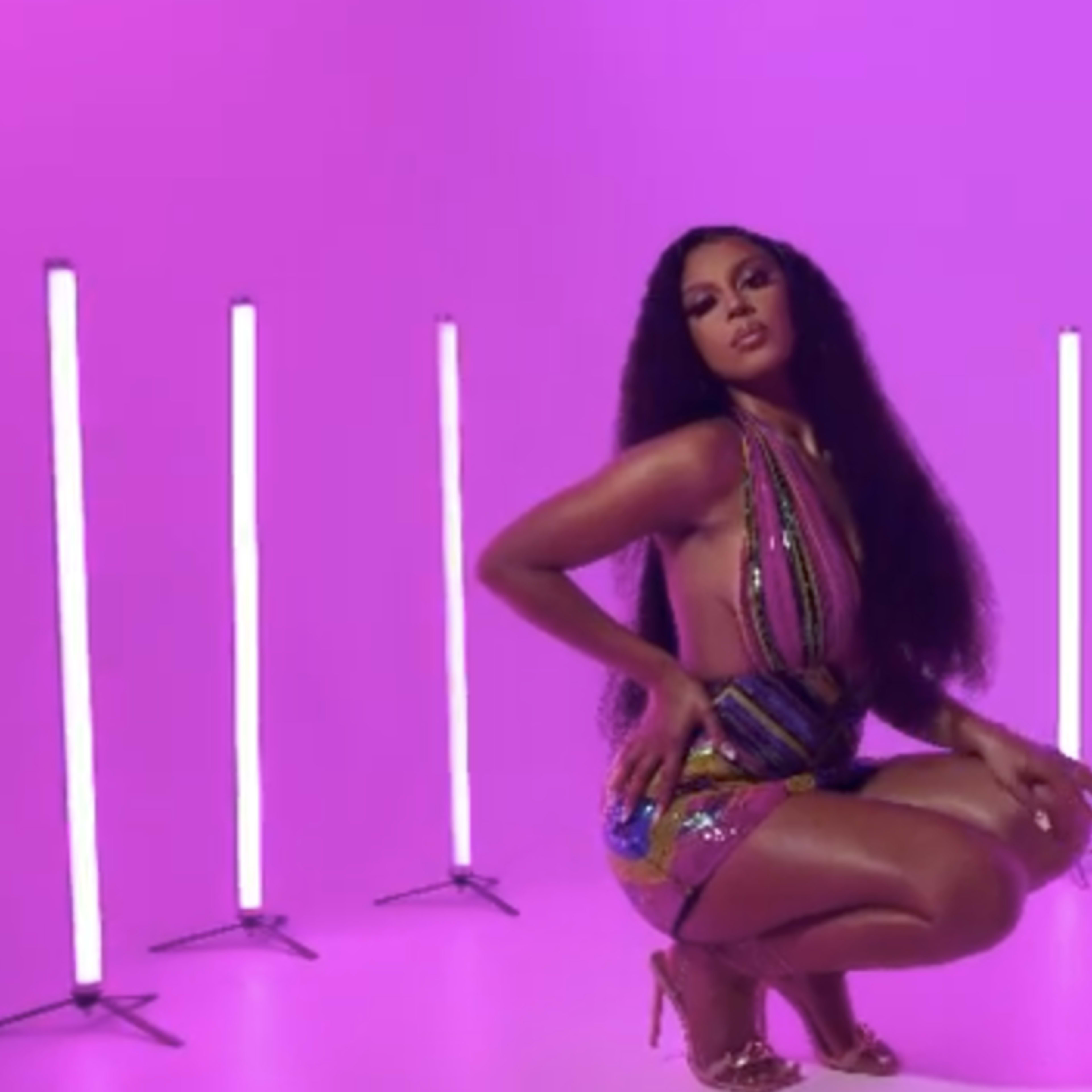 A woman poses in a colorful dress surrounded by vertical neon lights against a purple backdrop.
