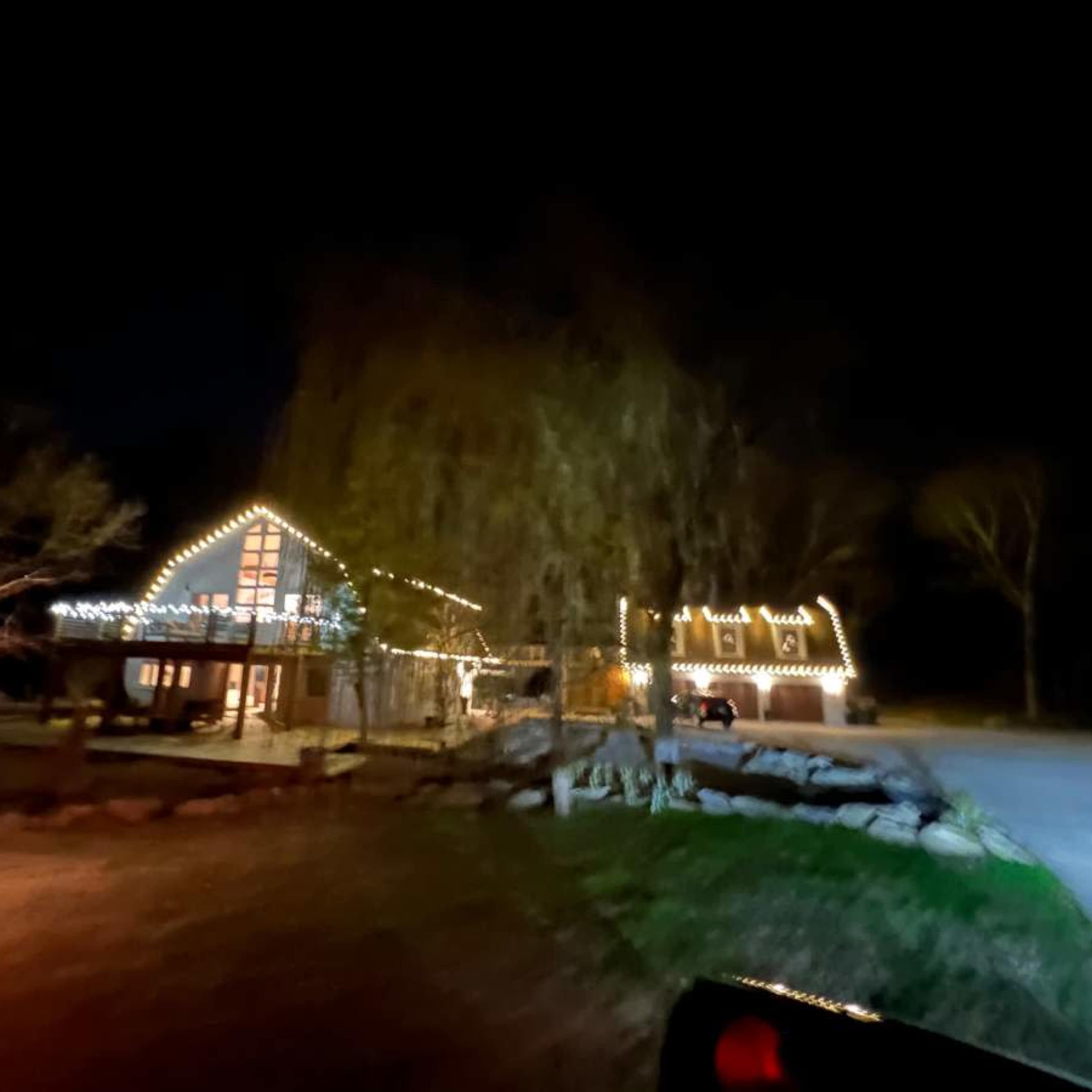 A house with decorative string lights is visible at night, surrounded by trees and a driveway.
