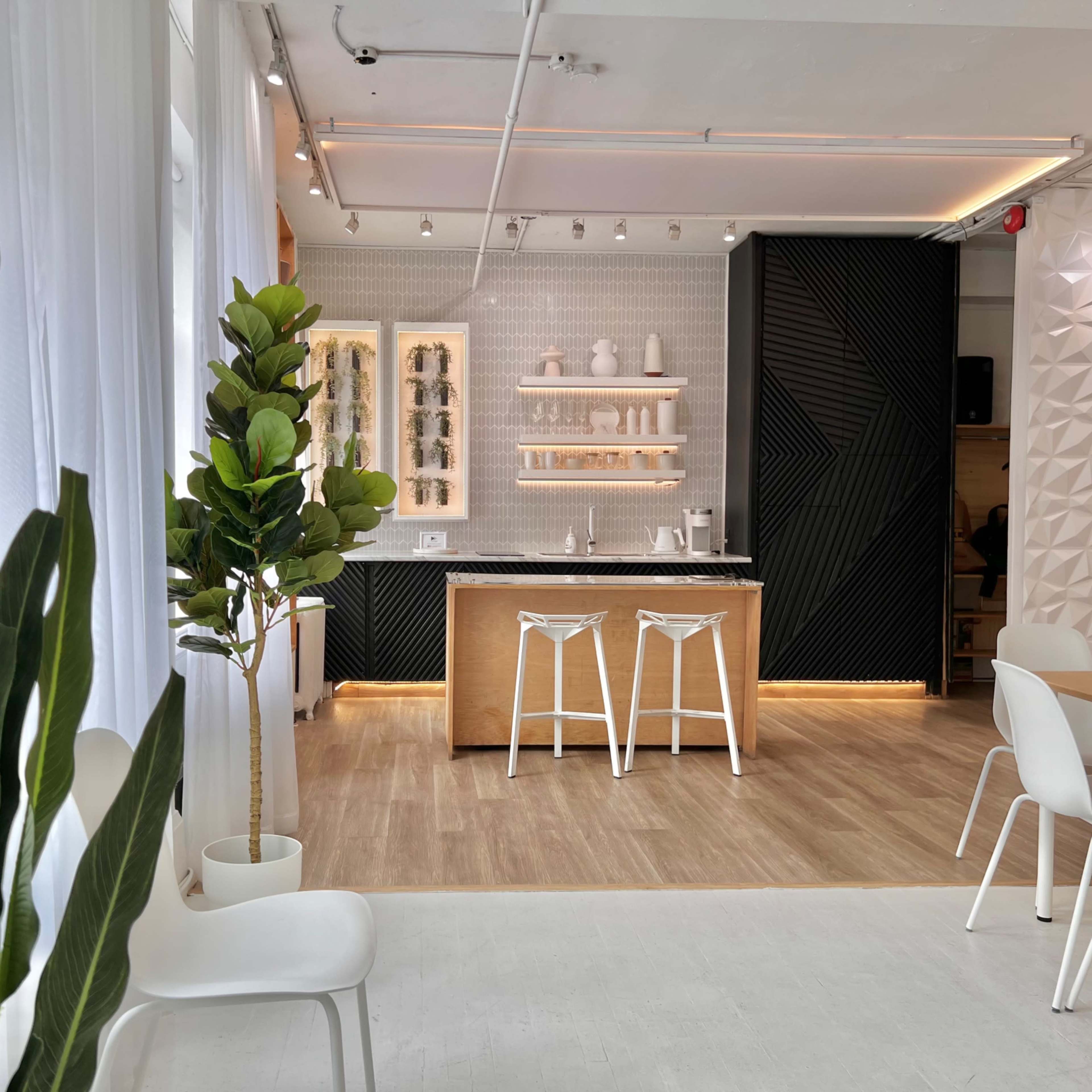 A modern interior space featuring a kitchen area with wooden accents, white chairs, and decorative plants.