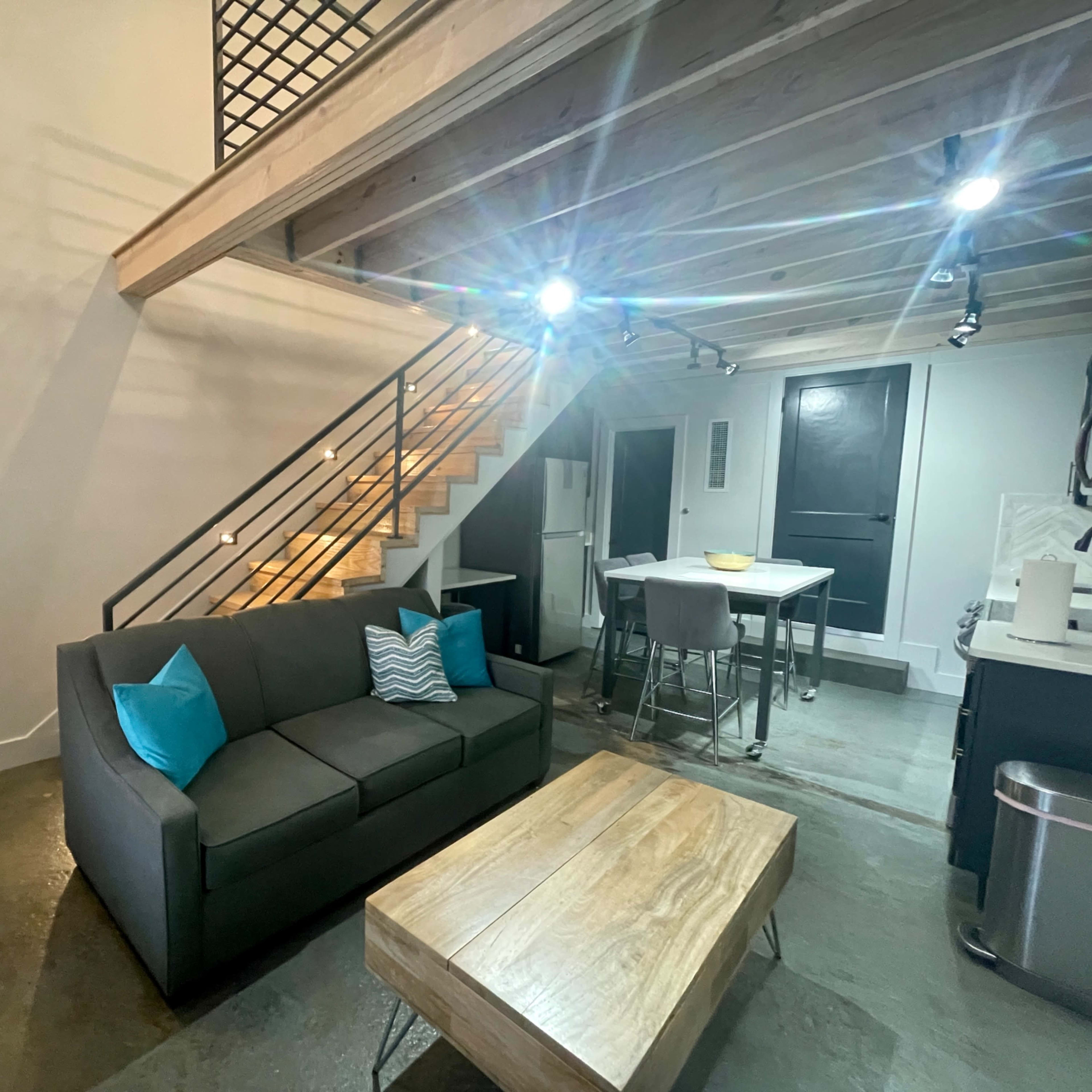 A modern living space featuring a gray sofa with teal cushions, a wooden coffee table, and a staircase leading to an upper level.