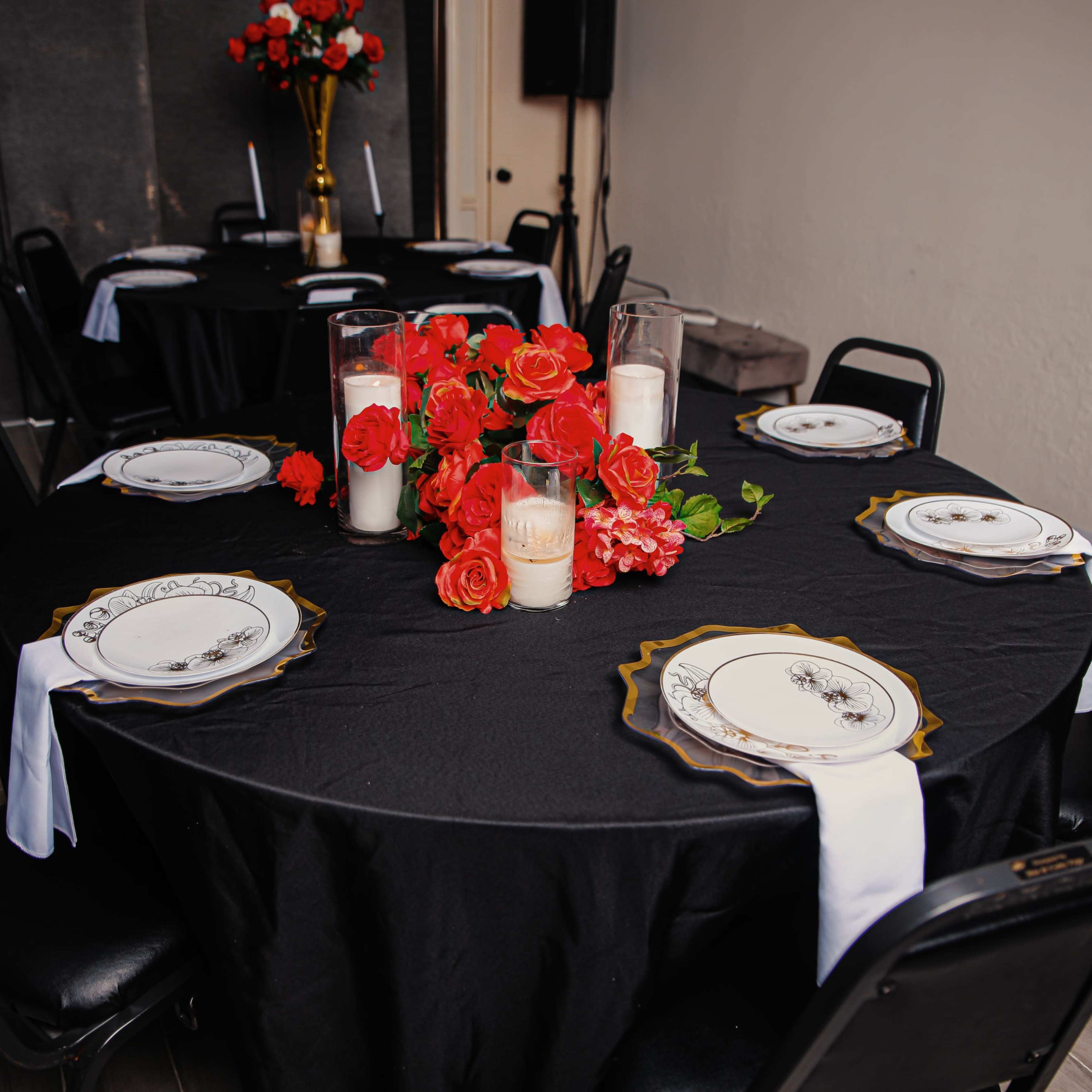 A black tablecloth covers a round table, set with decorative plates and a centerpiece of roses and candles.