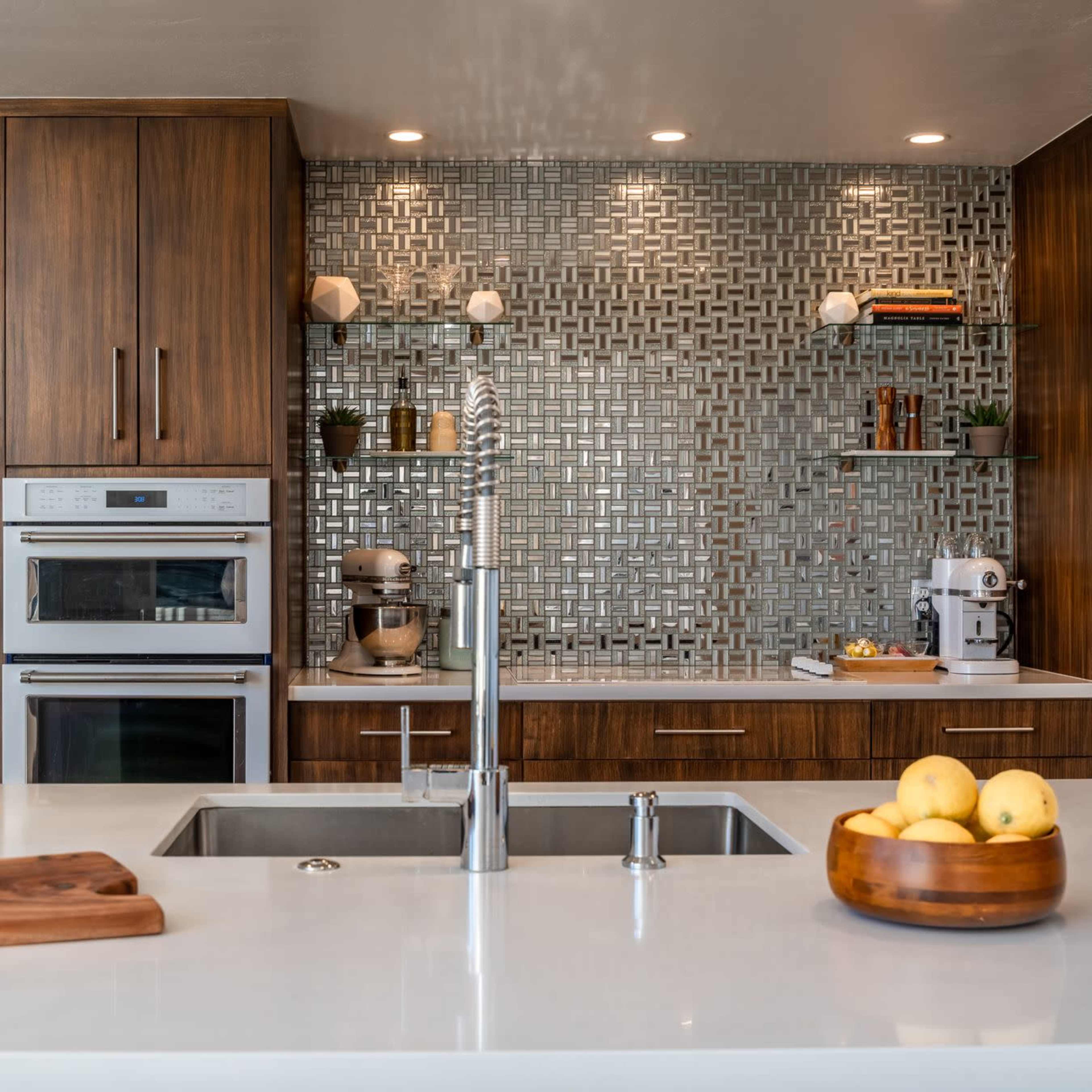 A modern kitchen with wooden cabinetry, a tile backsplash, and a central island featuring a sink and a bowl of lemons.