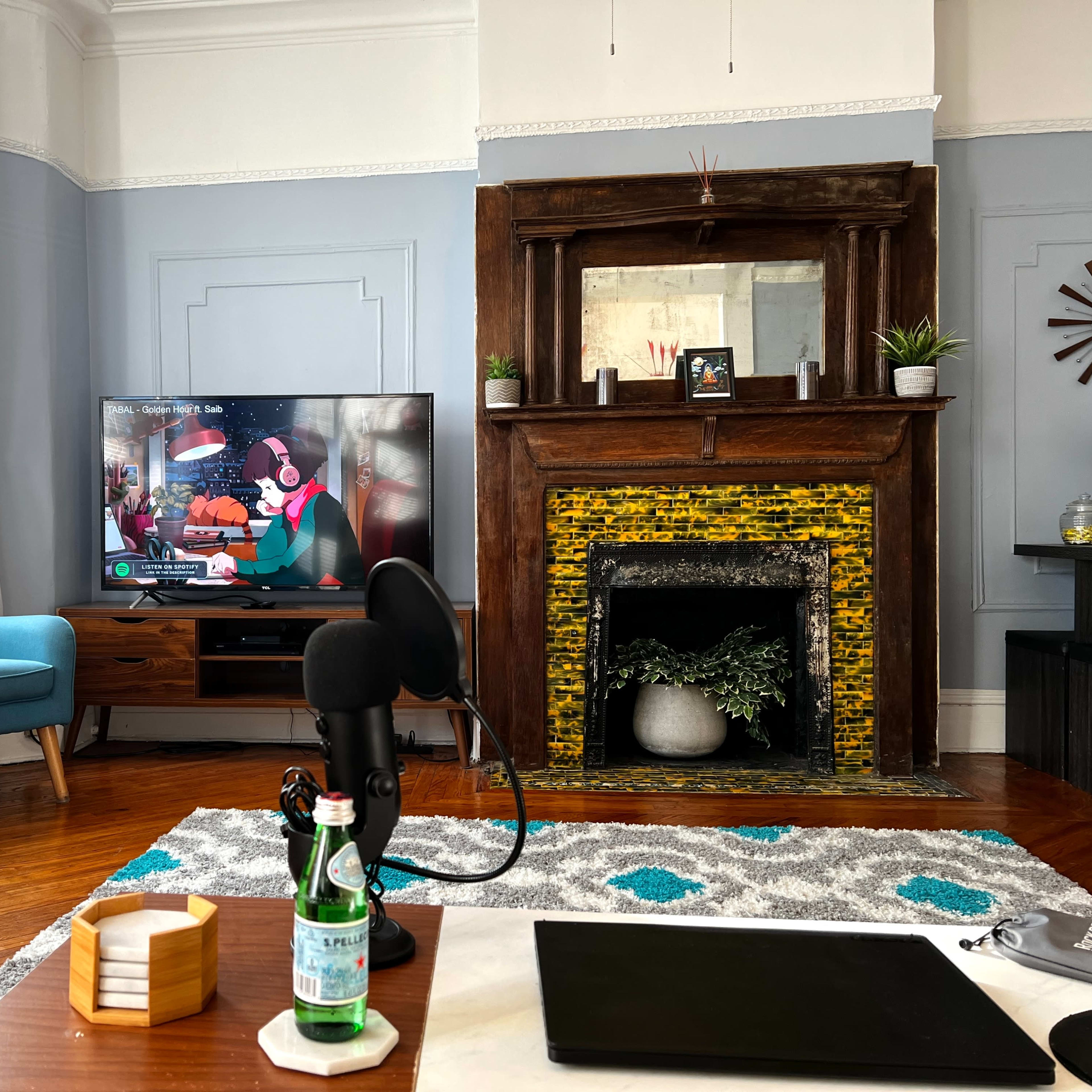 A living room features a television displaying a colorful scene, a vintage fireplace with a wooden mantel, and modern furniture including a coffee table and chairs.