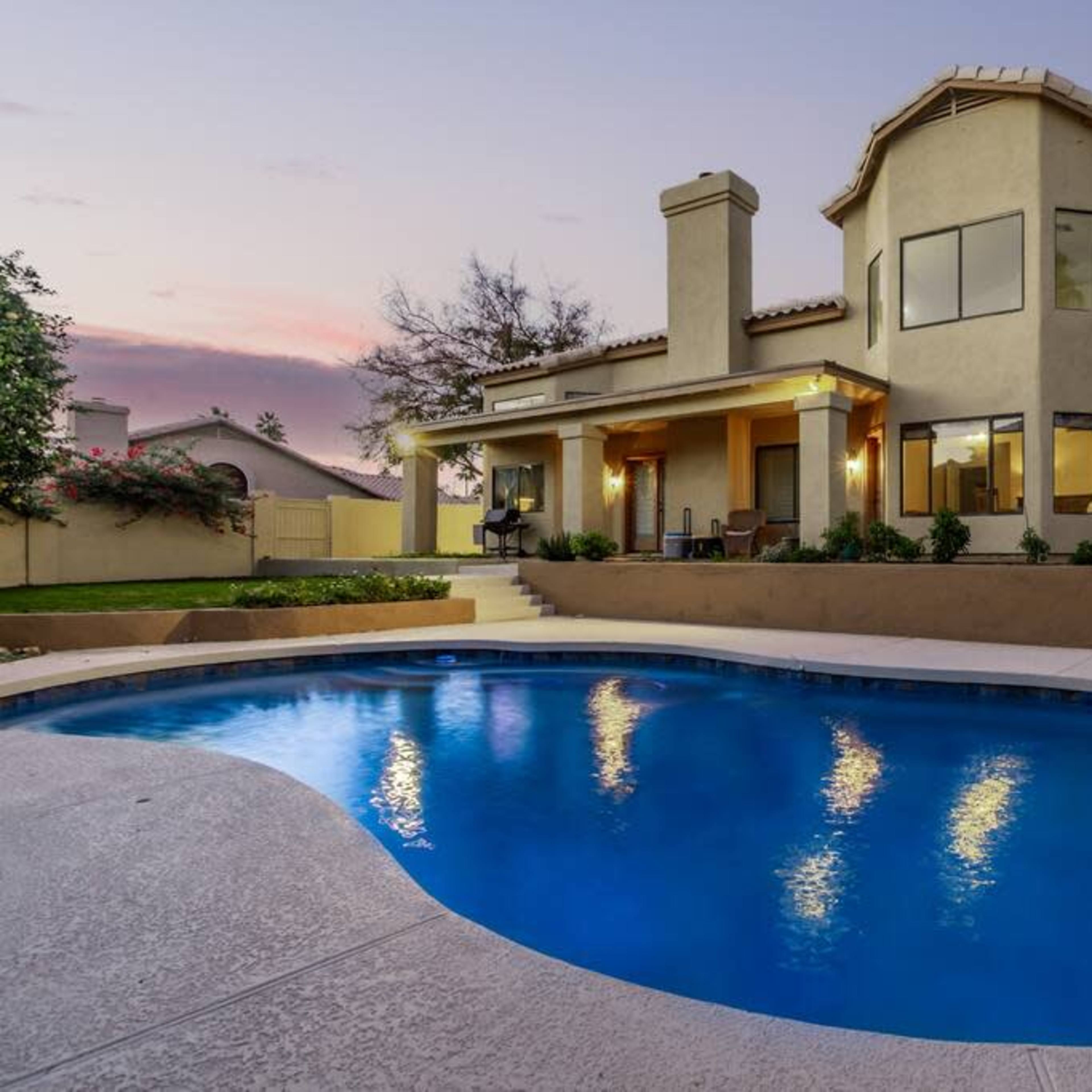 A modern house with a swimming pool in the backyard is illuminated by the evening sky.