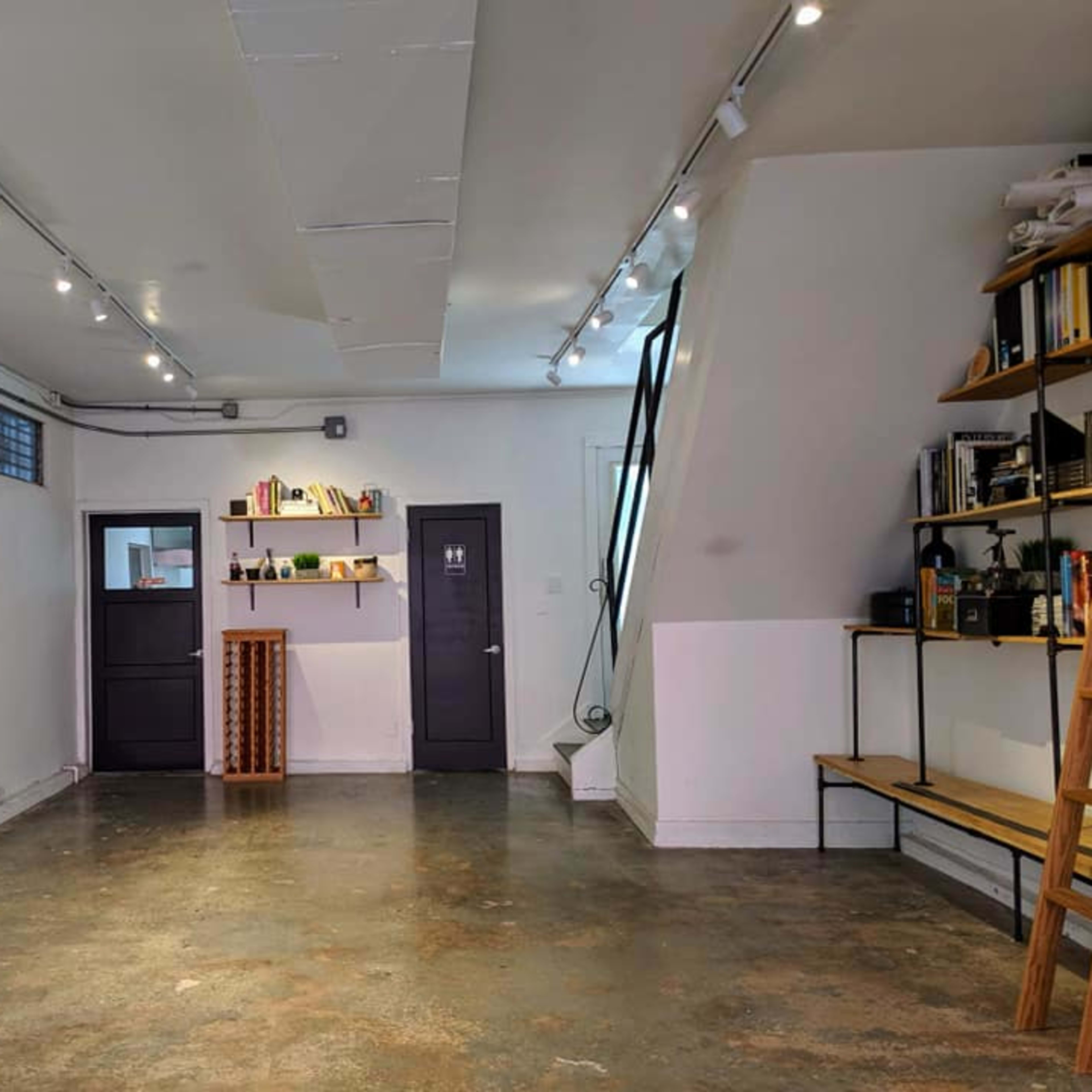 A spacious, minimalist room with concrete flooring, featuring shelves and a small display area against one wall.