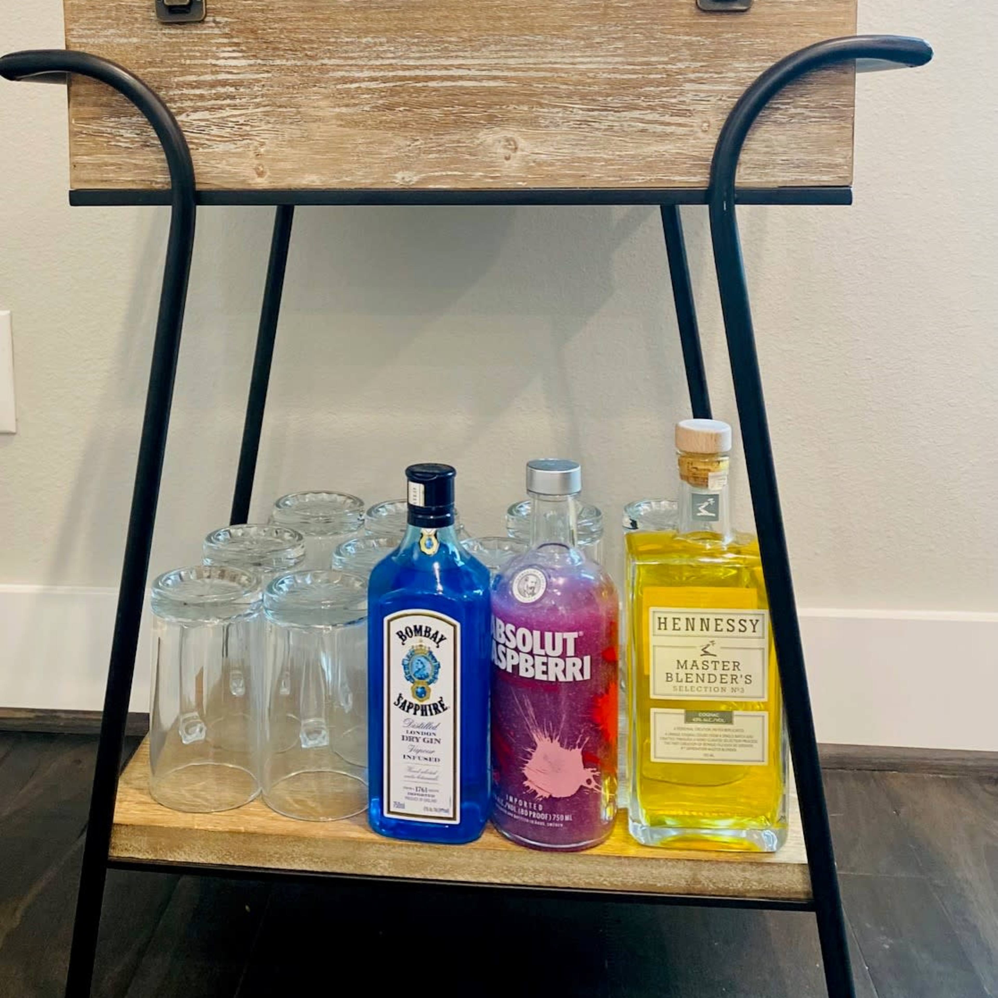 A wooden bar cart displays various bottles of alcohol and glassware, along with a framed sign that reads, "I just rescued some wine... it was trapped in a bottle."
