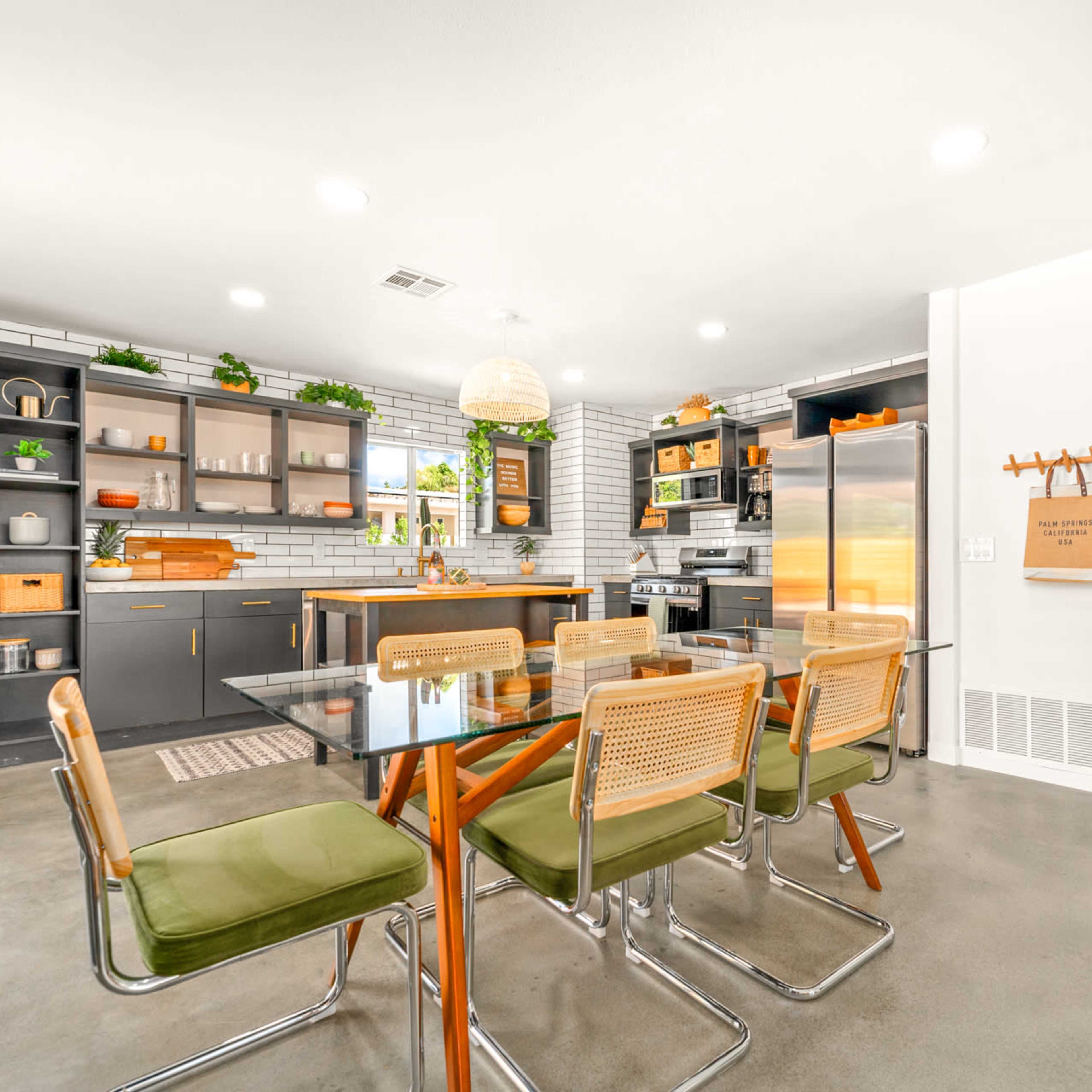 A modern kitchen and dining area features a glass table with green chairs, alongside sleek cabinetry and stainless steel appliances.