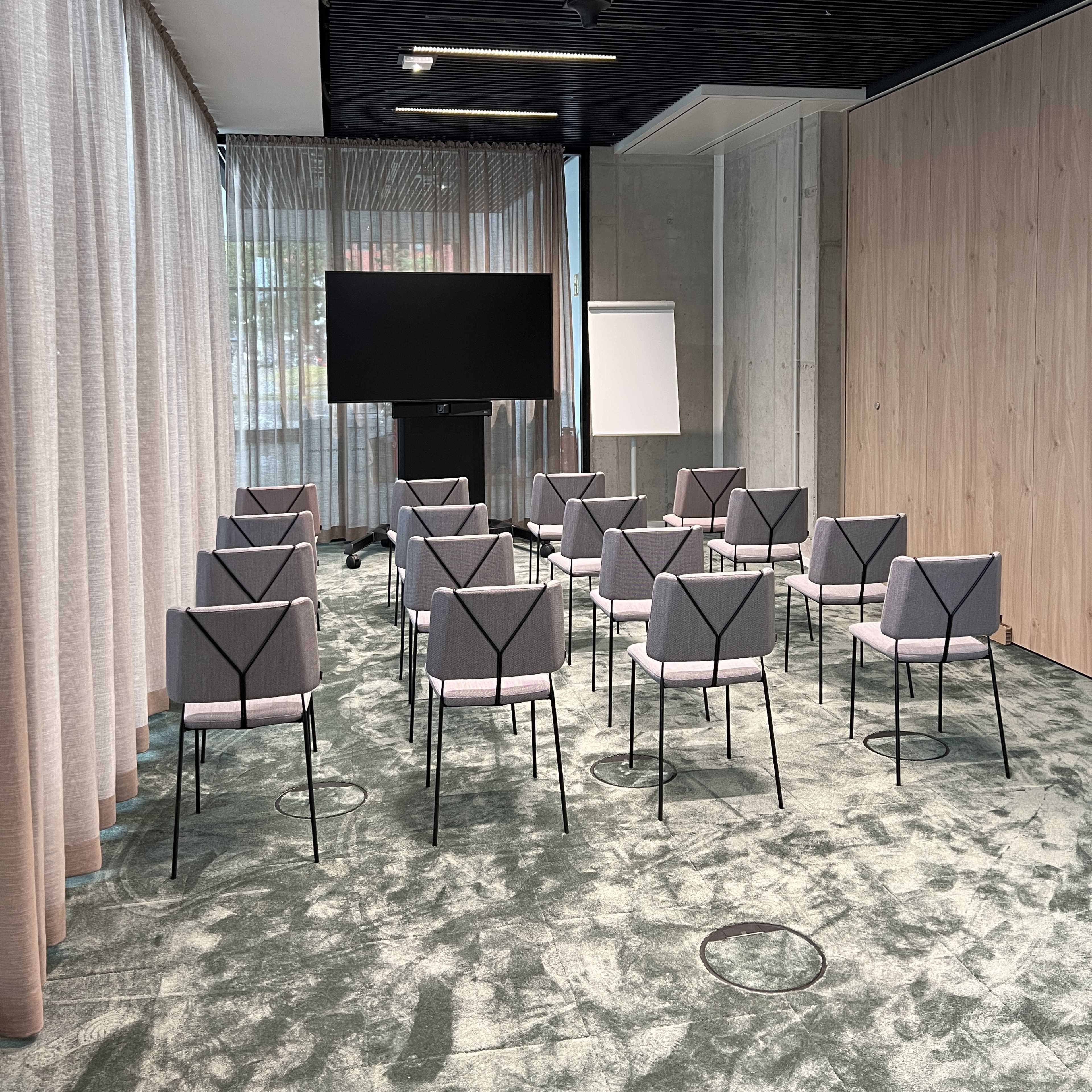 A meeting room with several rows of chairs arranged facing a large screen and a flip chart.