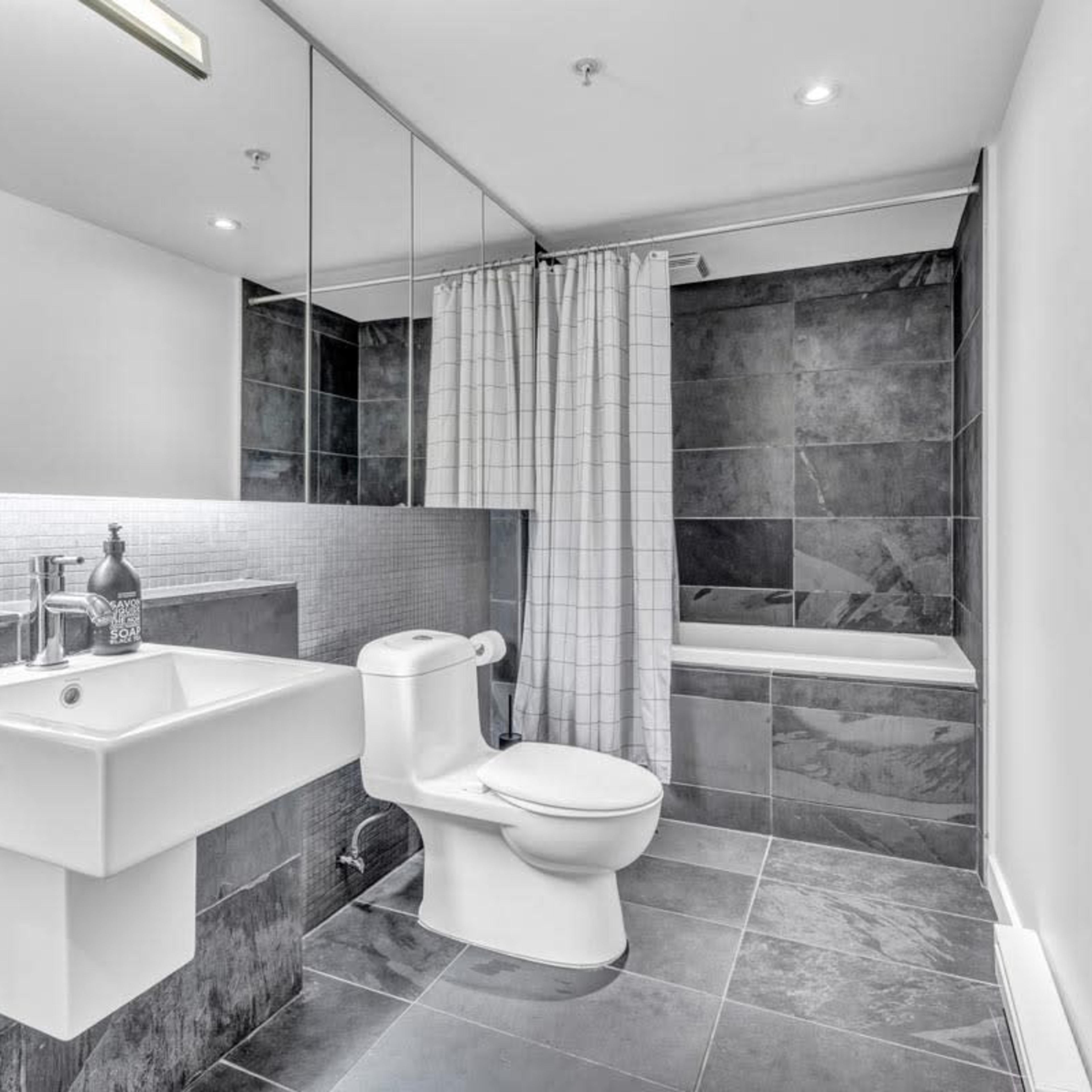 The bathroom features a modern design with a sink, toilet, and a bathtub surrounded by gray tiles and a curtain.