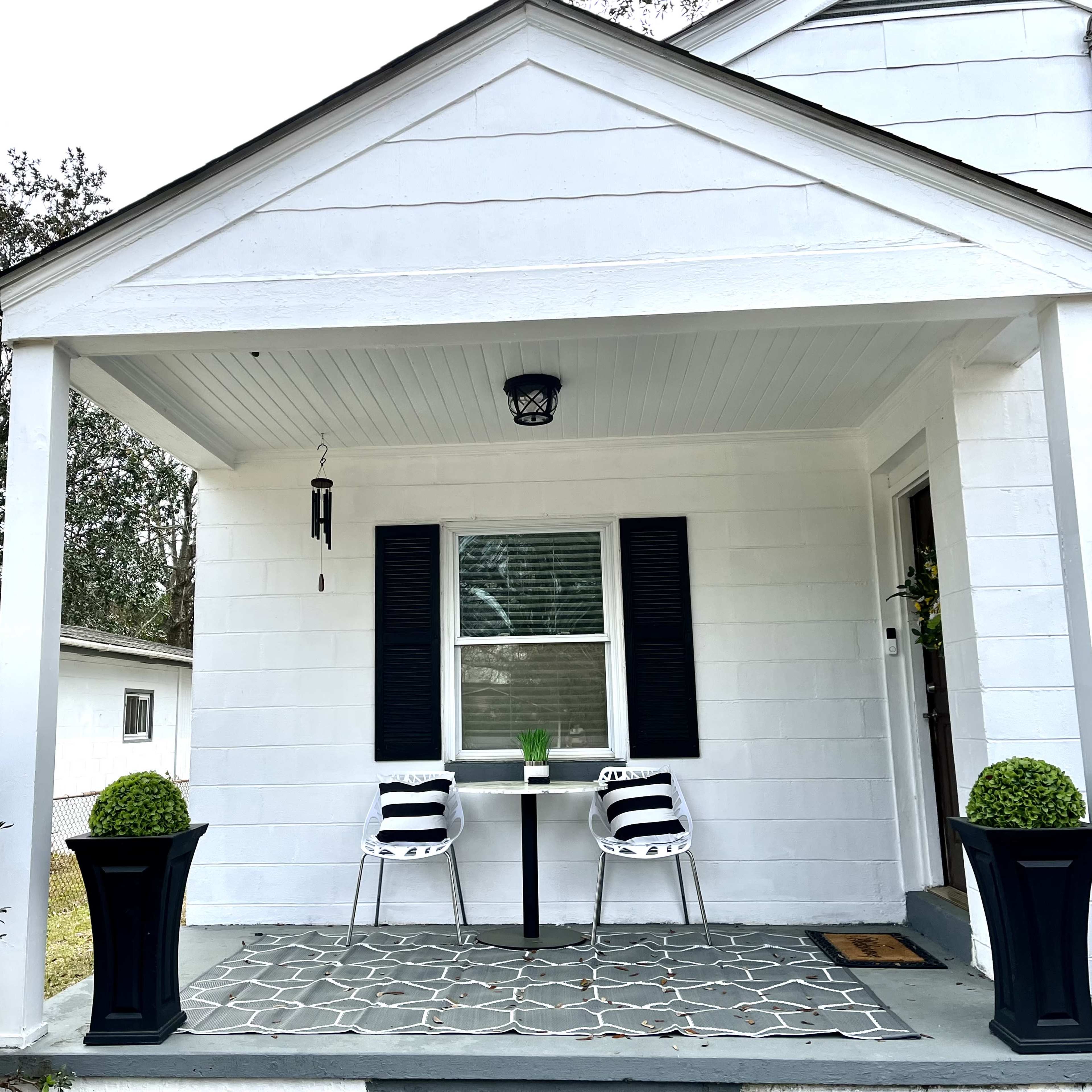 A white front porch with two black-and-white striped chairs, a small table, and potted plants on either side.