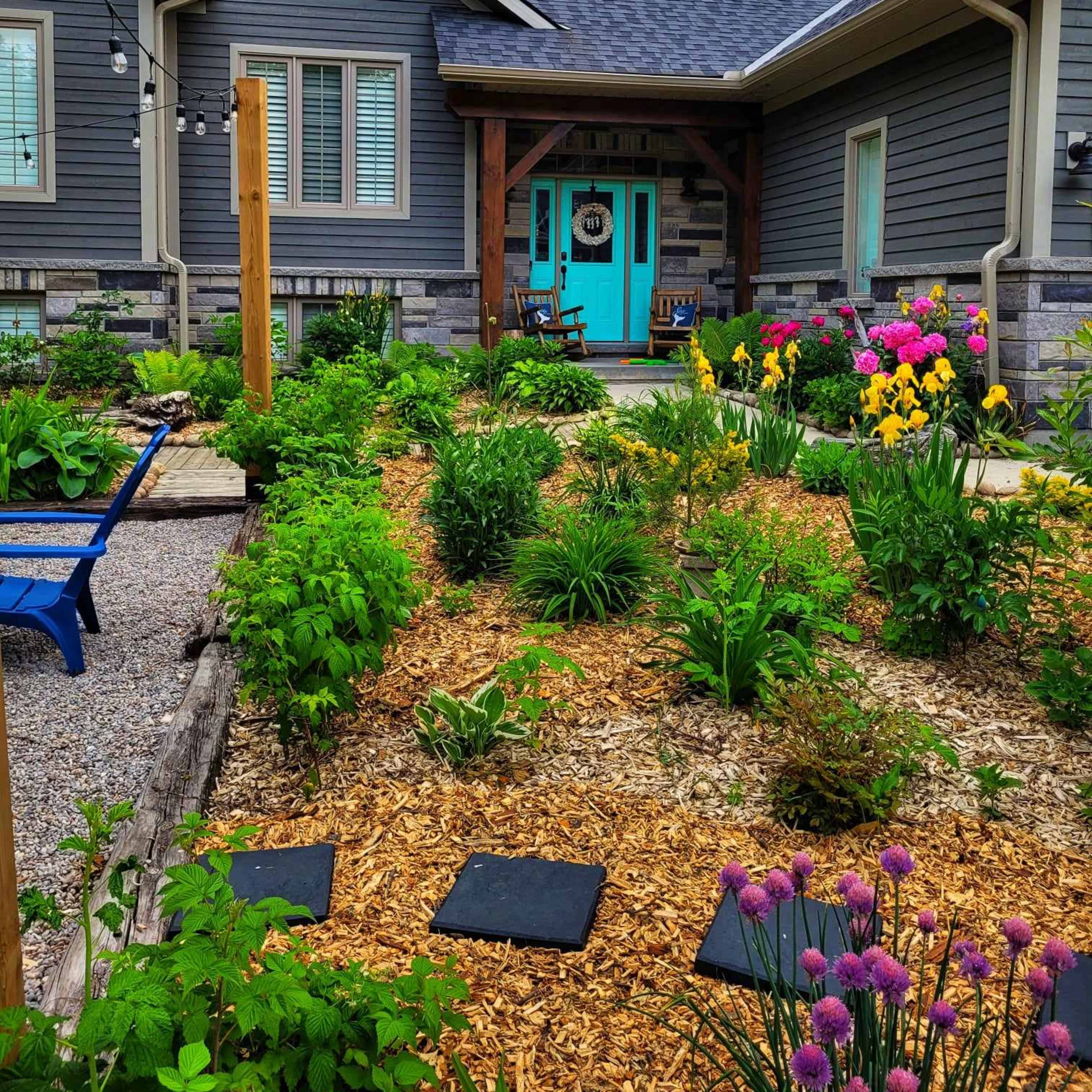 A well-maintained garden with colorful flowers and greenery surrounds a modern home featuring a blue front door.