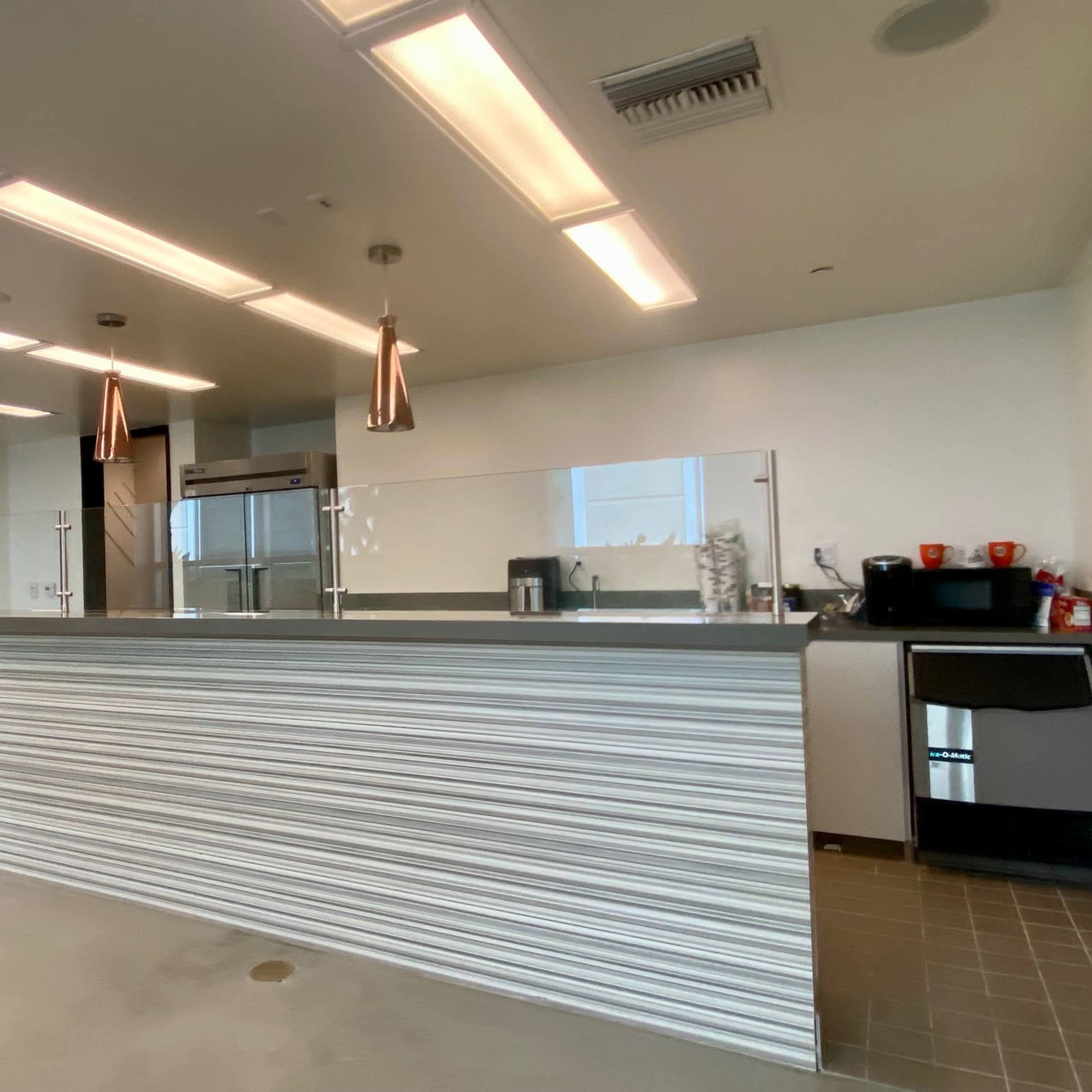 A modern kitchen area with a gray countertop, pendant lighting, and a coffee station on one side.