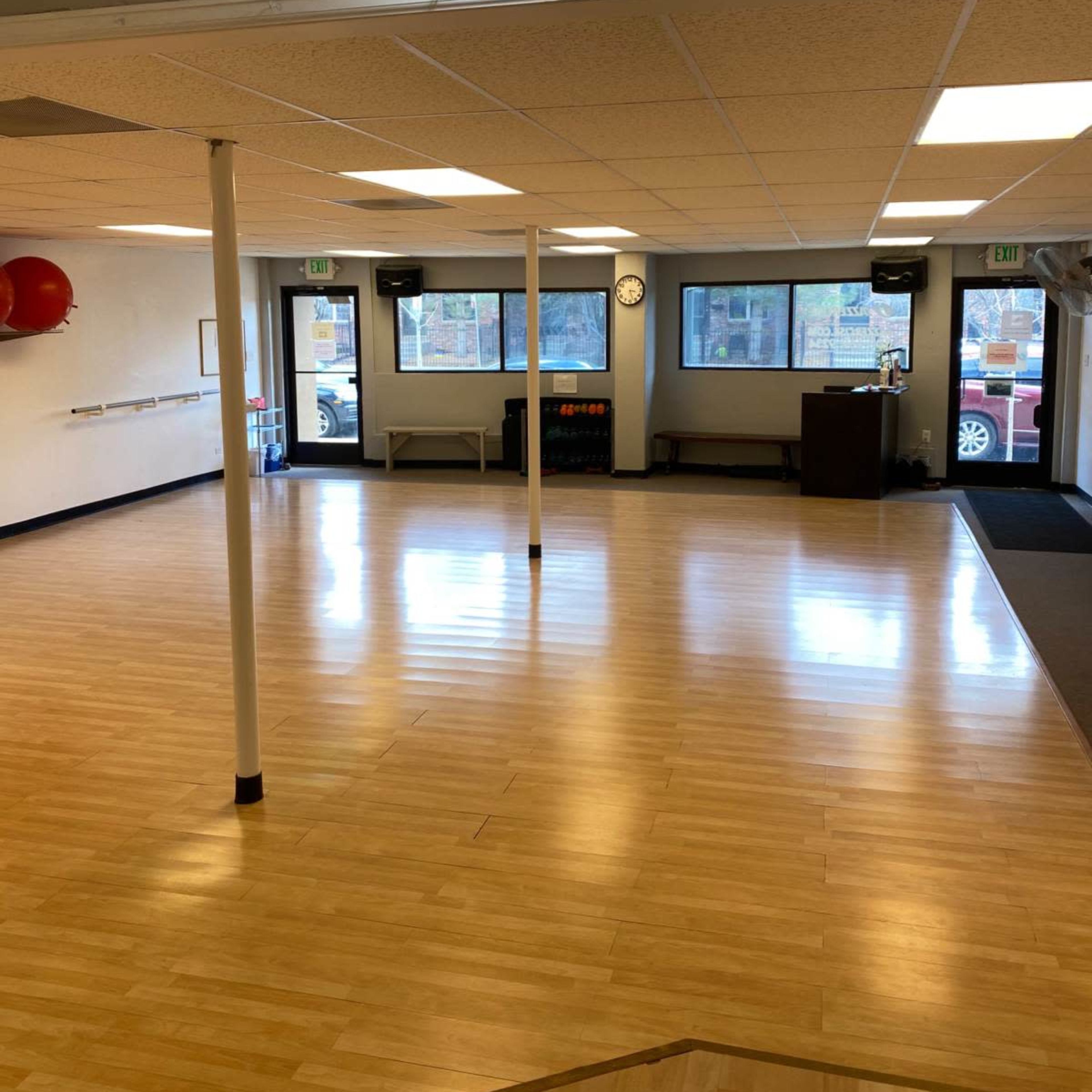 A spacious, empty room with wooden flooring, large windows, and minimal furnishings.