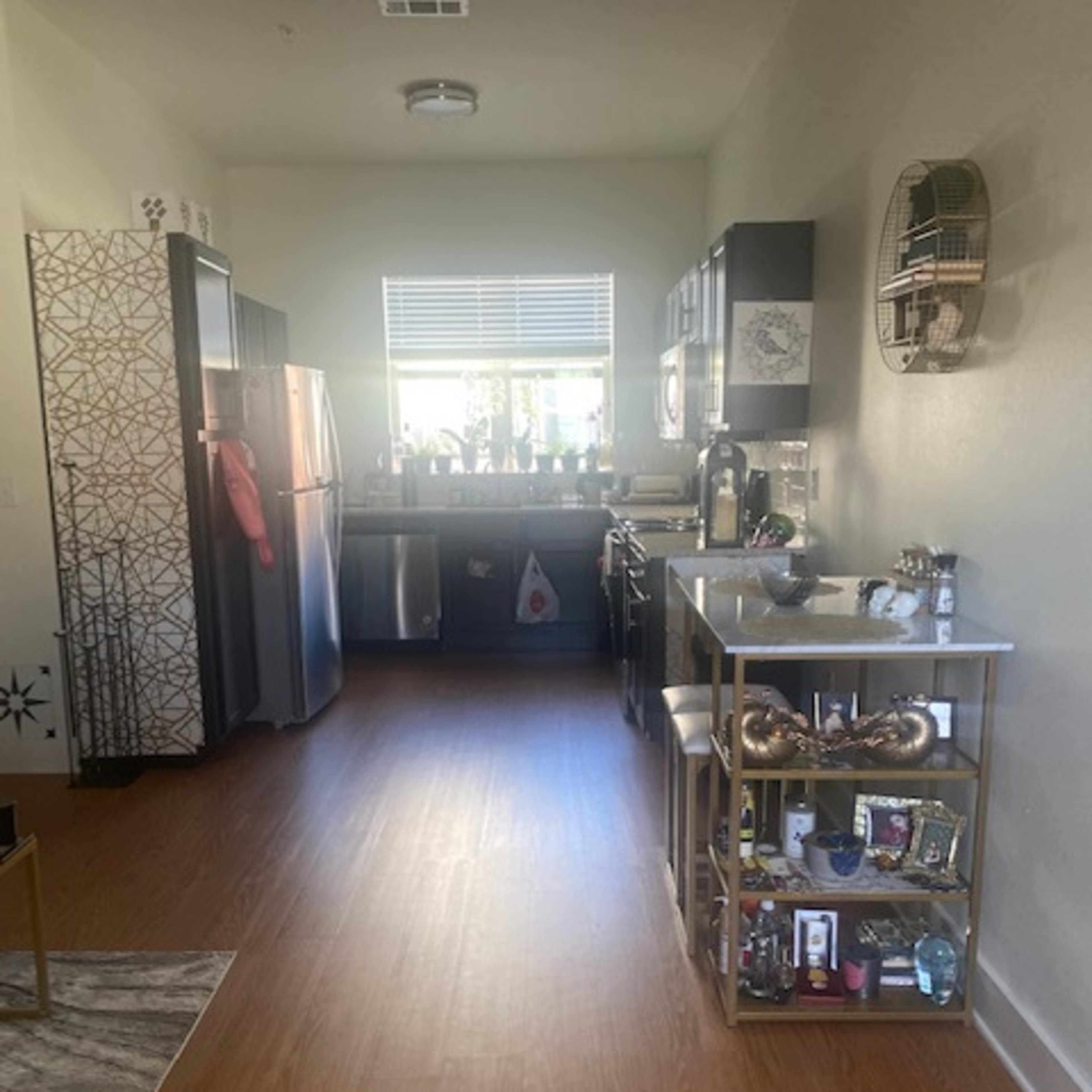 A modern kitchen features stainless steel appliances, a central island cart, and hardwood flooring.