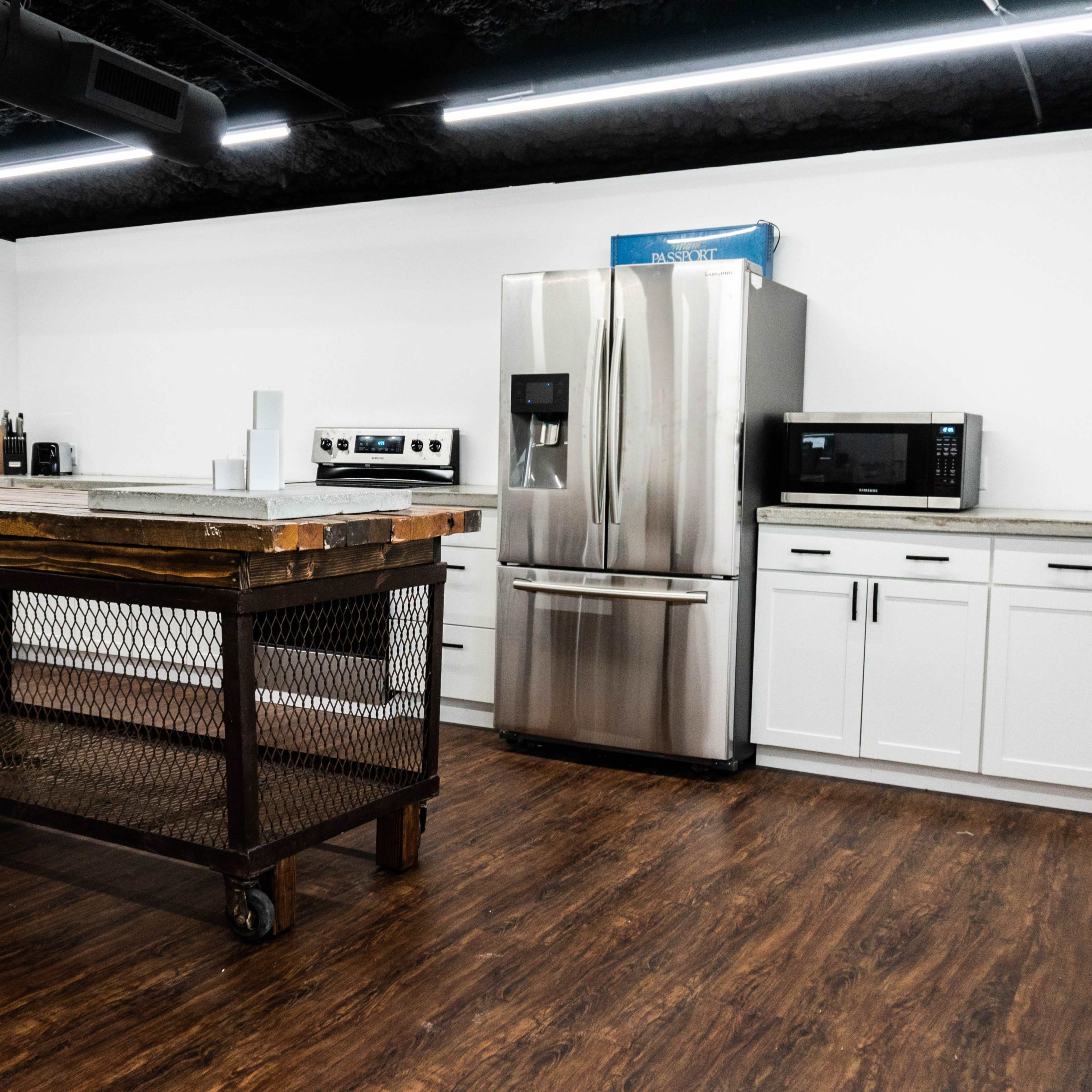 A modern kitchen features stainless steel appliances, a large industrial-style island on wheels, and white cabinetry against a dark ceiling.