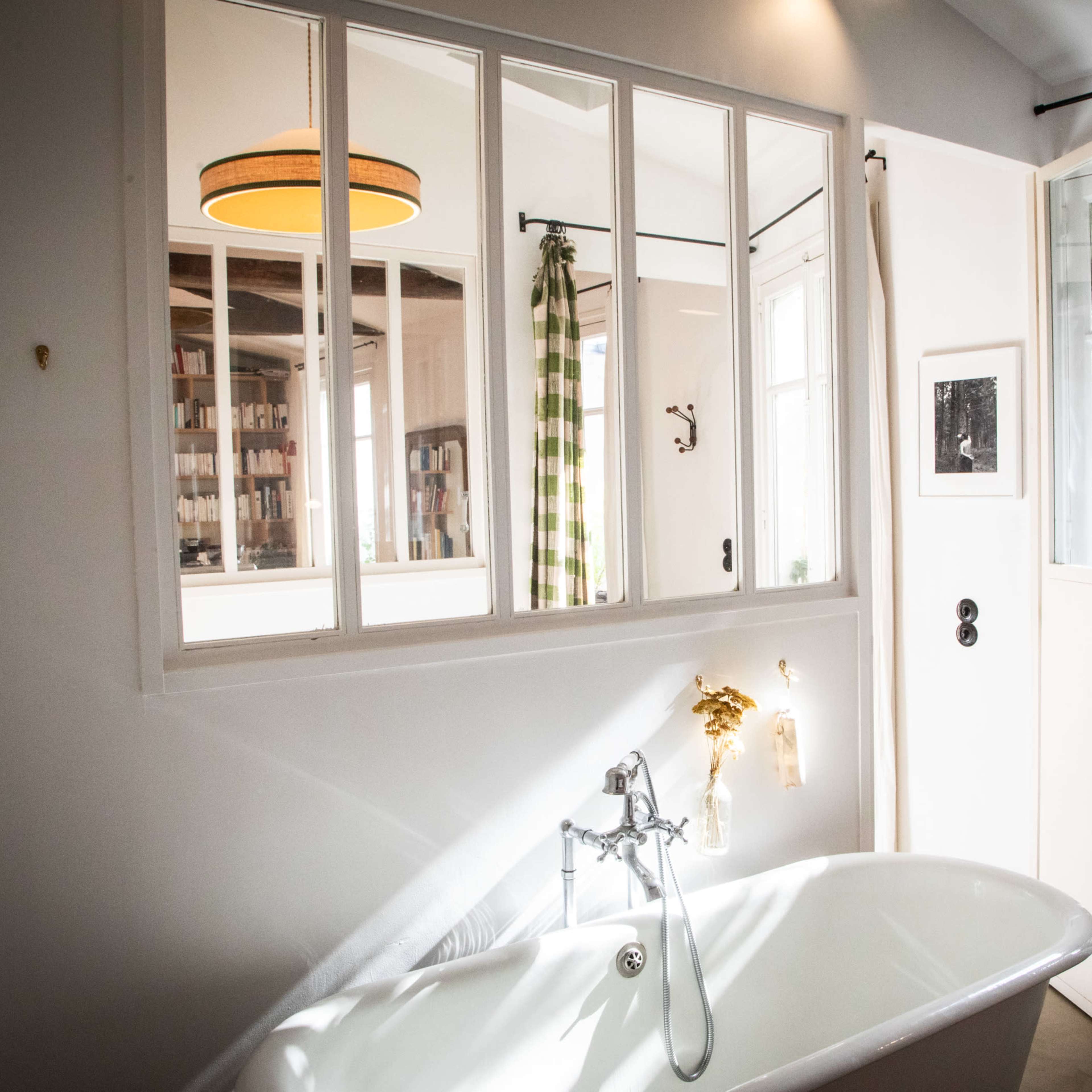 A bright bathroom features a freestanding bathtub, large windows, and a shower curtain with a checkered pattern.