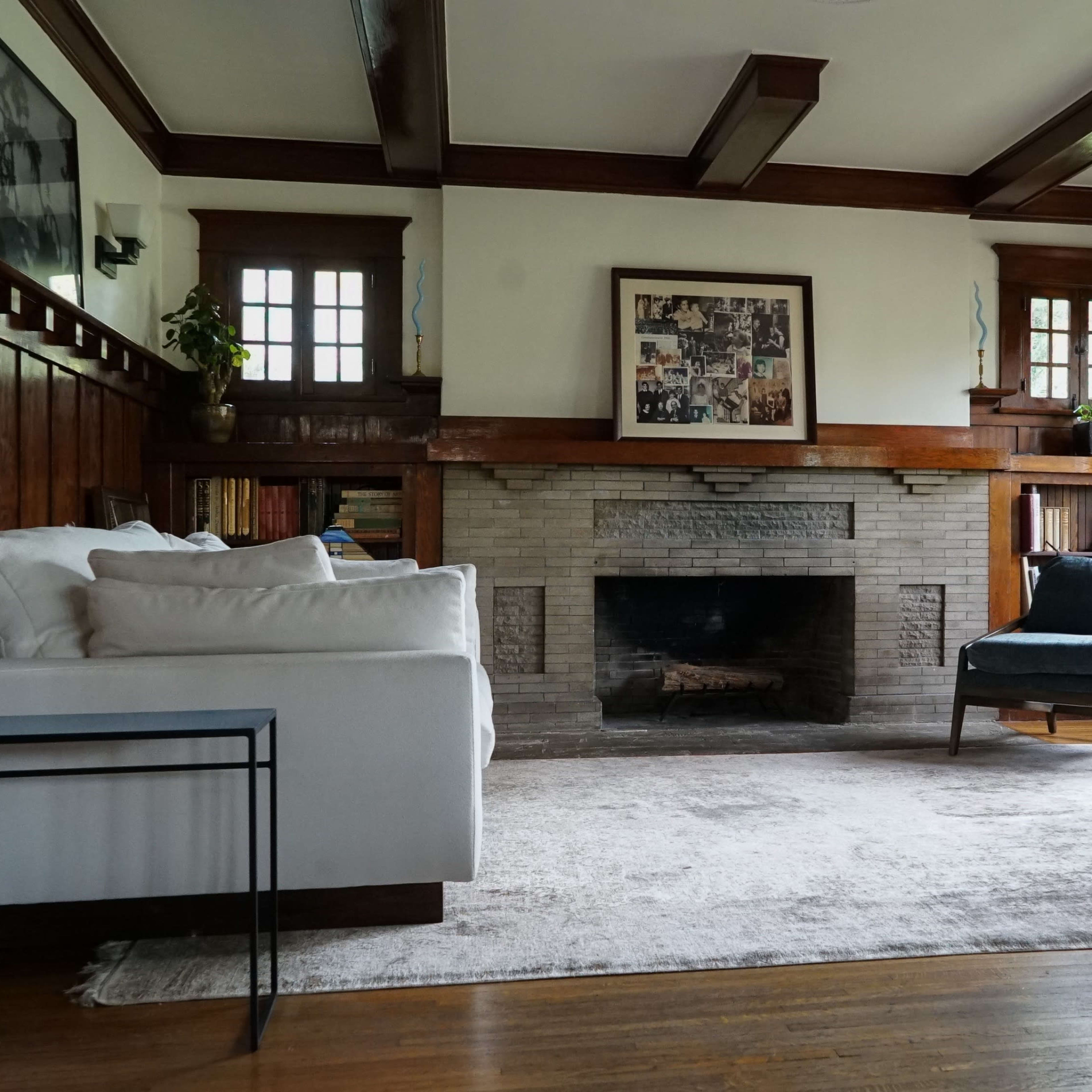 The living room features a white sofa and a blue armchair facing a stone fireplace, with wooden beams and built-in bookshelves lining the walls.