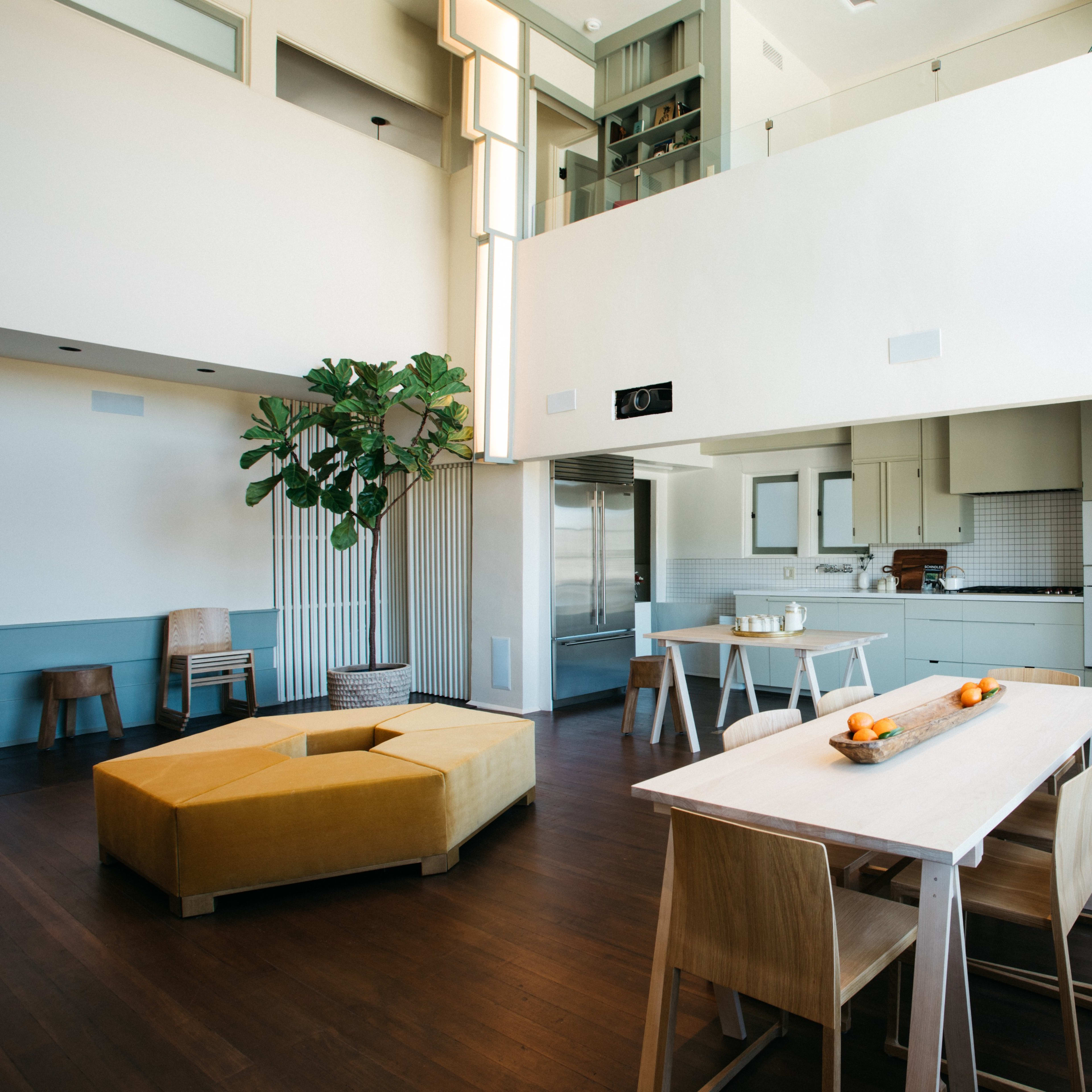 A modern, open-concept kitchen and dining area with light-colored walls, wooden flooring, and large windows.