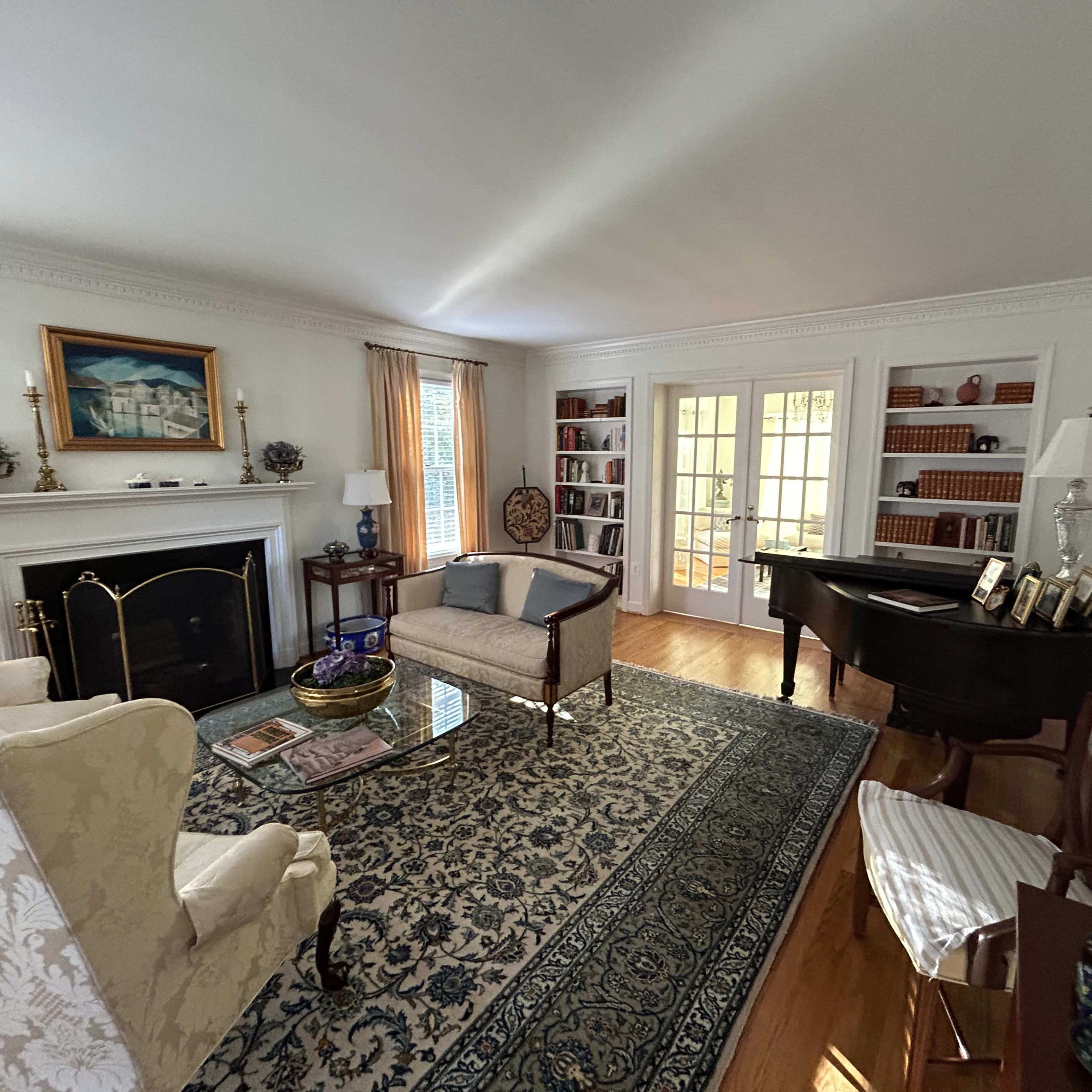 A tidy living room with a fireplace, a piano, bookshelves, and a large area rug.