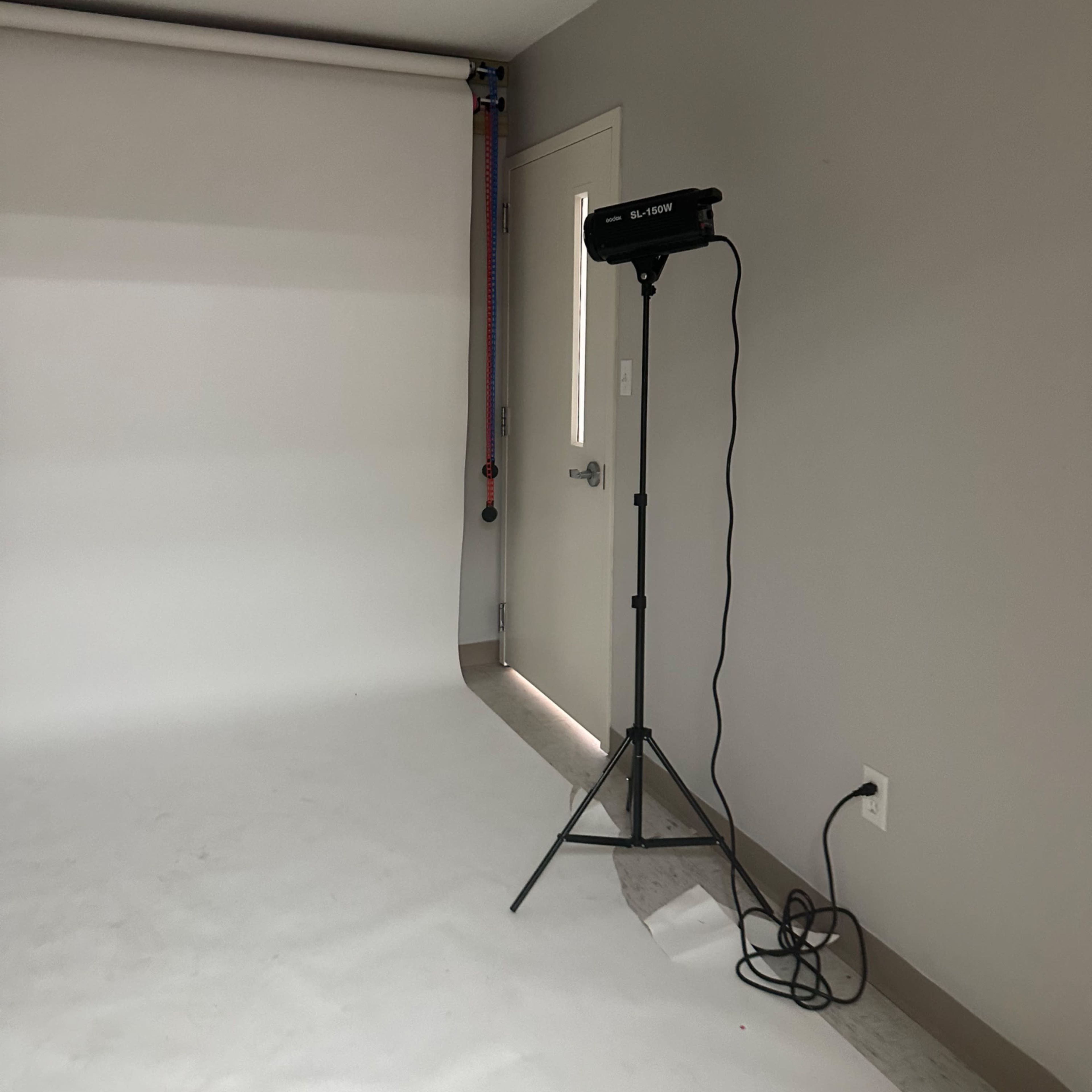 A photography studio with a blank backdrop, a light stand, and a door on the side.