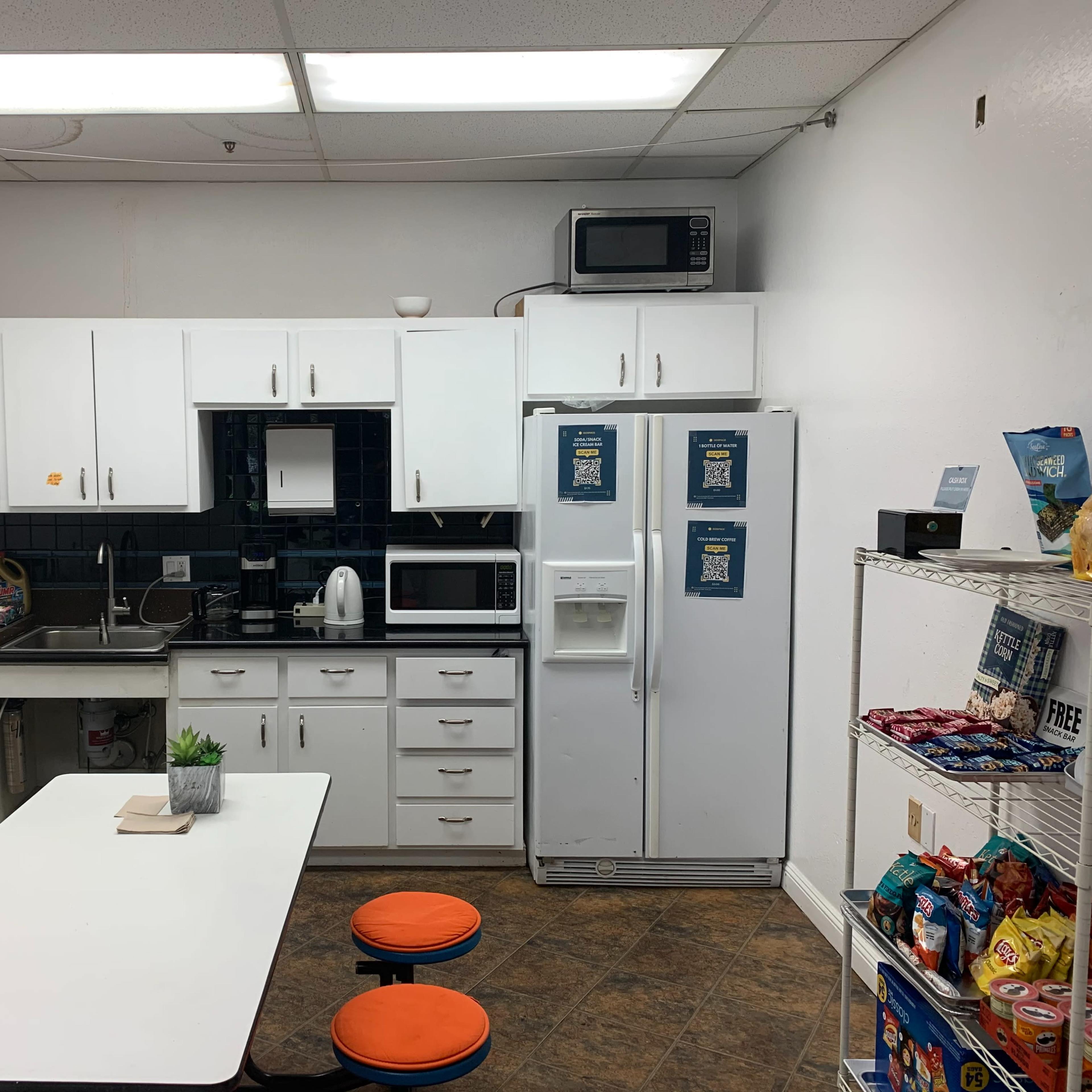 A small kitchen with white cabinets, a sink, a microwave, a refrigerator, and a table with two stools.