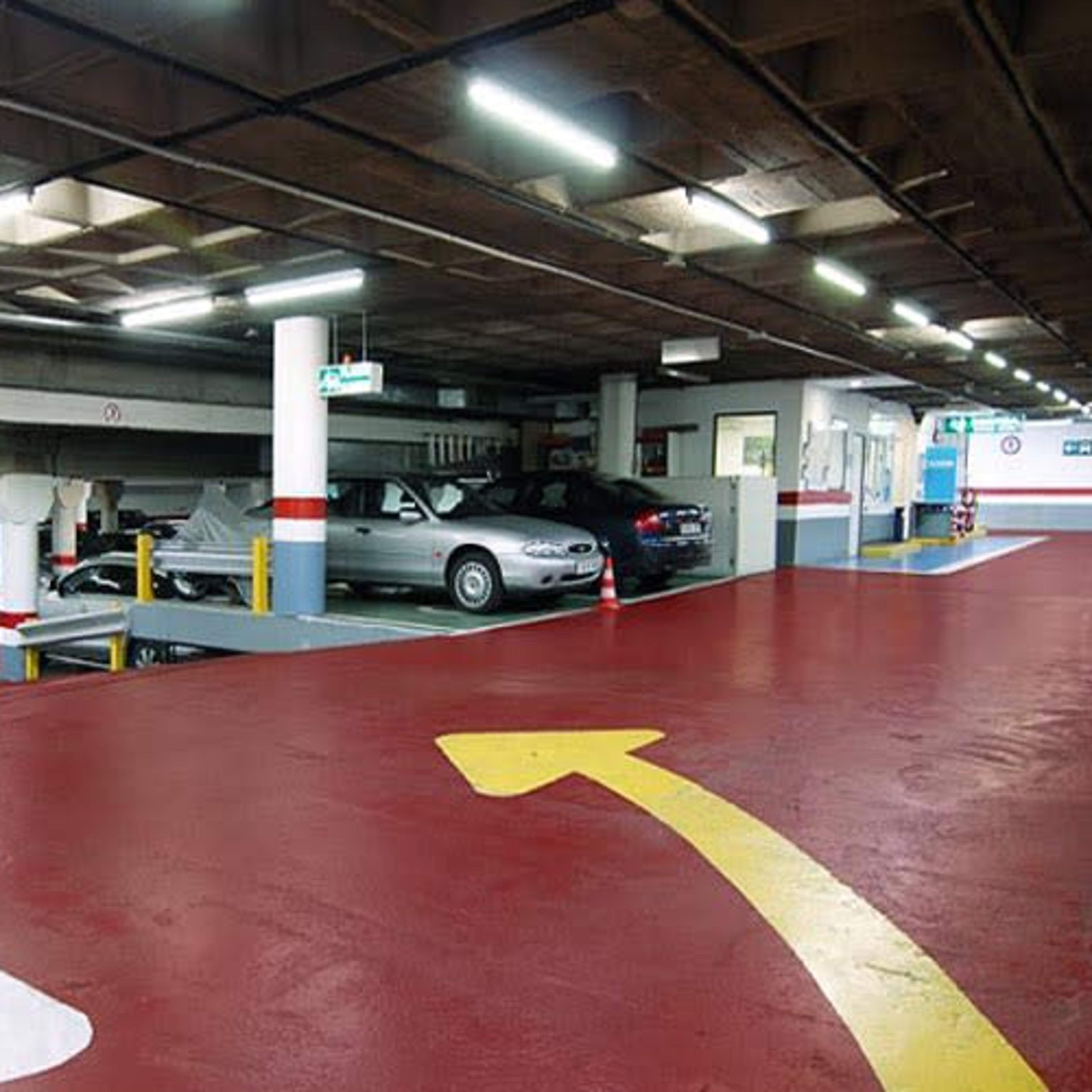 An empty parking garage with painted directional arrows and parked cars along the sides.