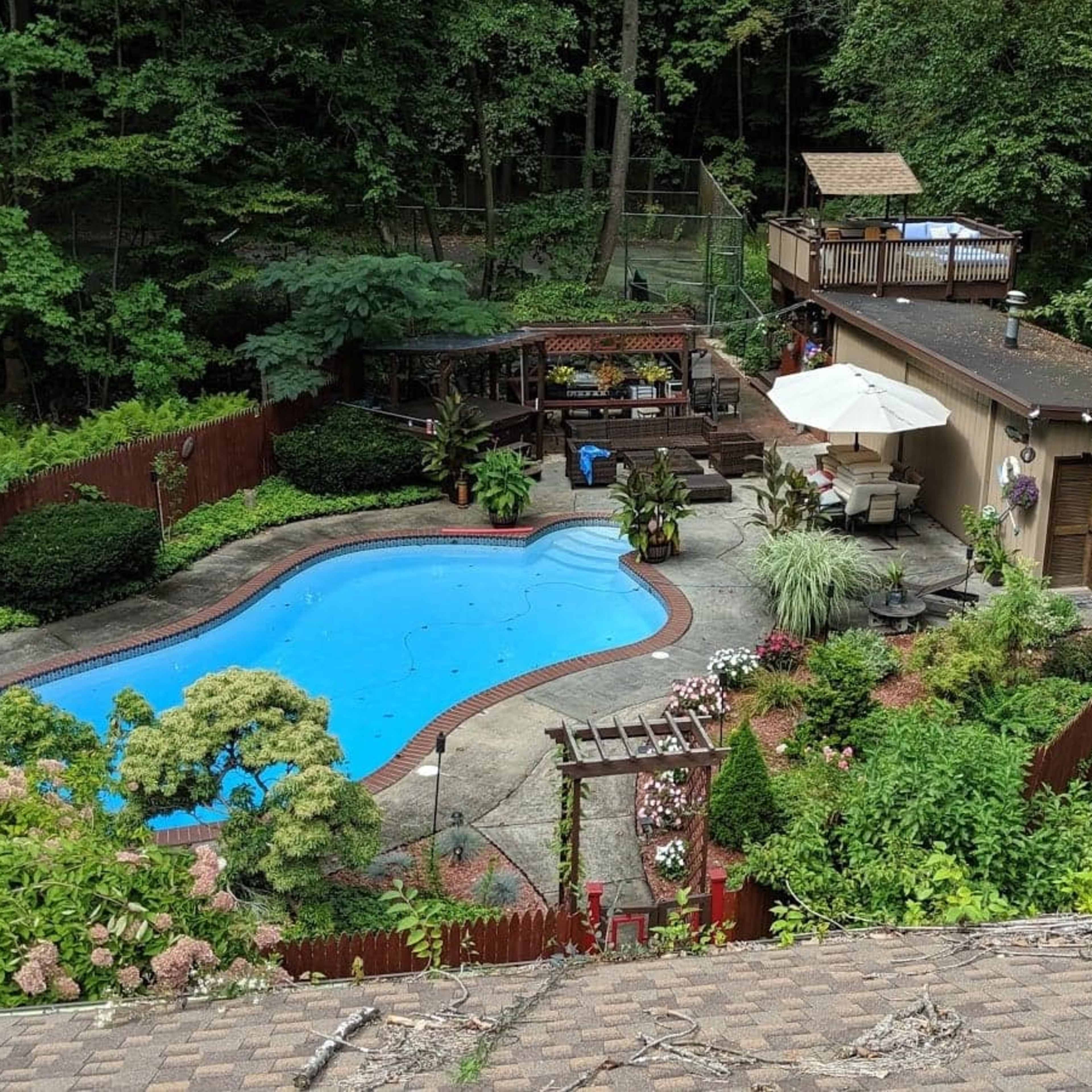A backyard with a swimming pool surrounded by landscaped gardens, a deck, and a house in a wooded area.