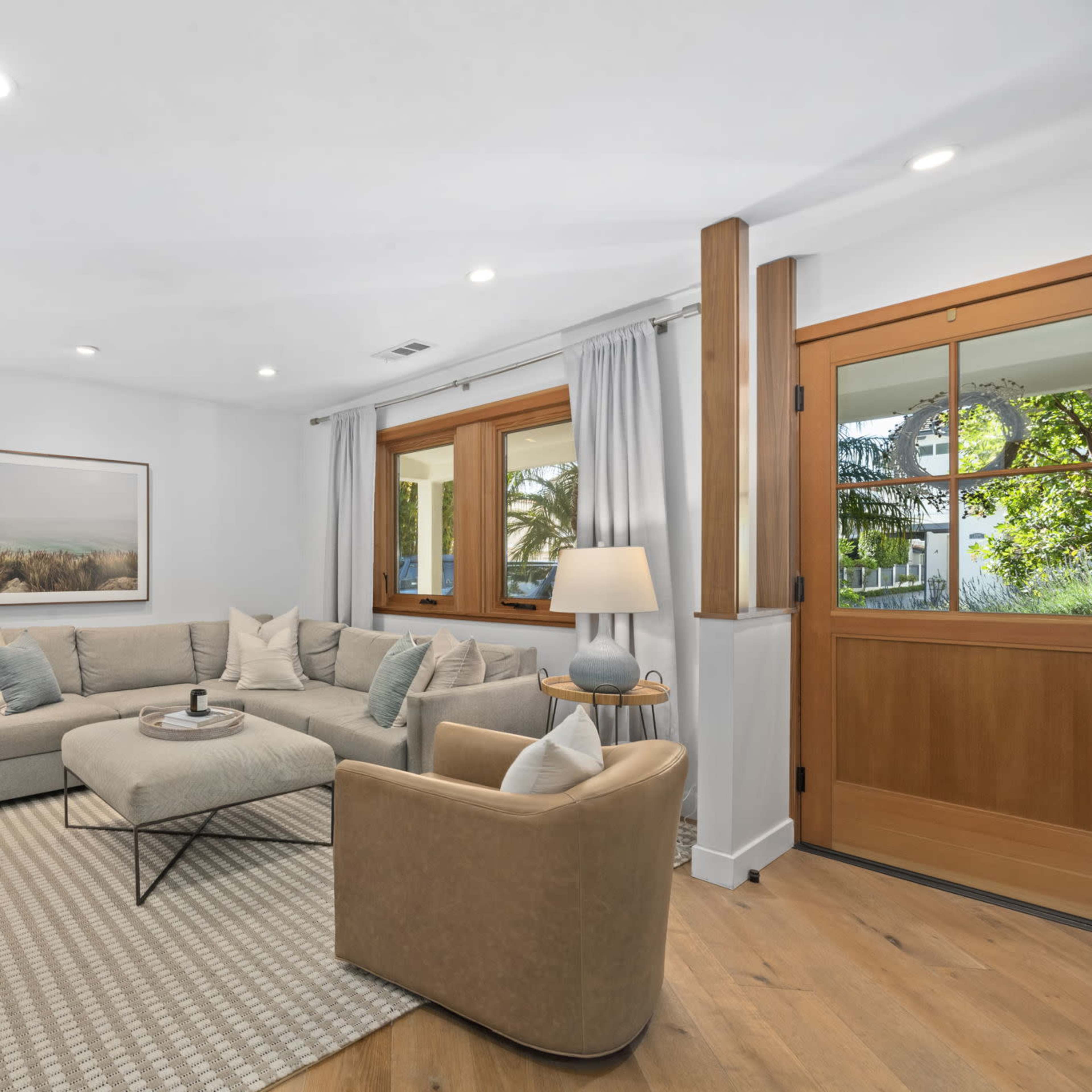 A modern living room features a sectional sofa, two armchairs, a coffee table, and large windows allowing natural light to enter.