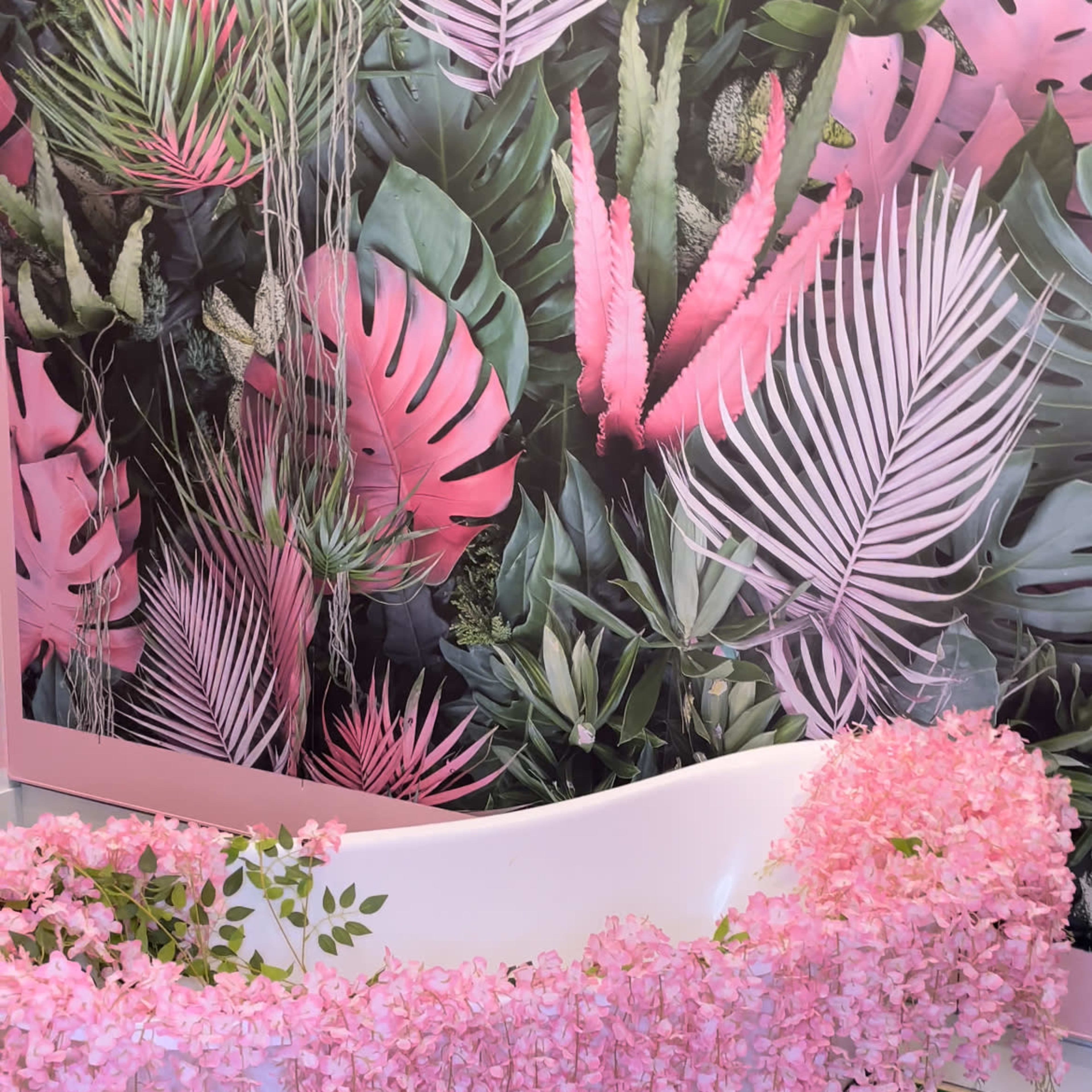 A white clawfoot bathtub is adorned with cascading pink flowers against a backdrop of tropical foliage and pink leaves.