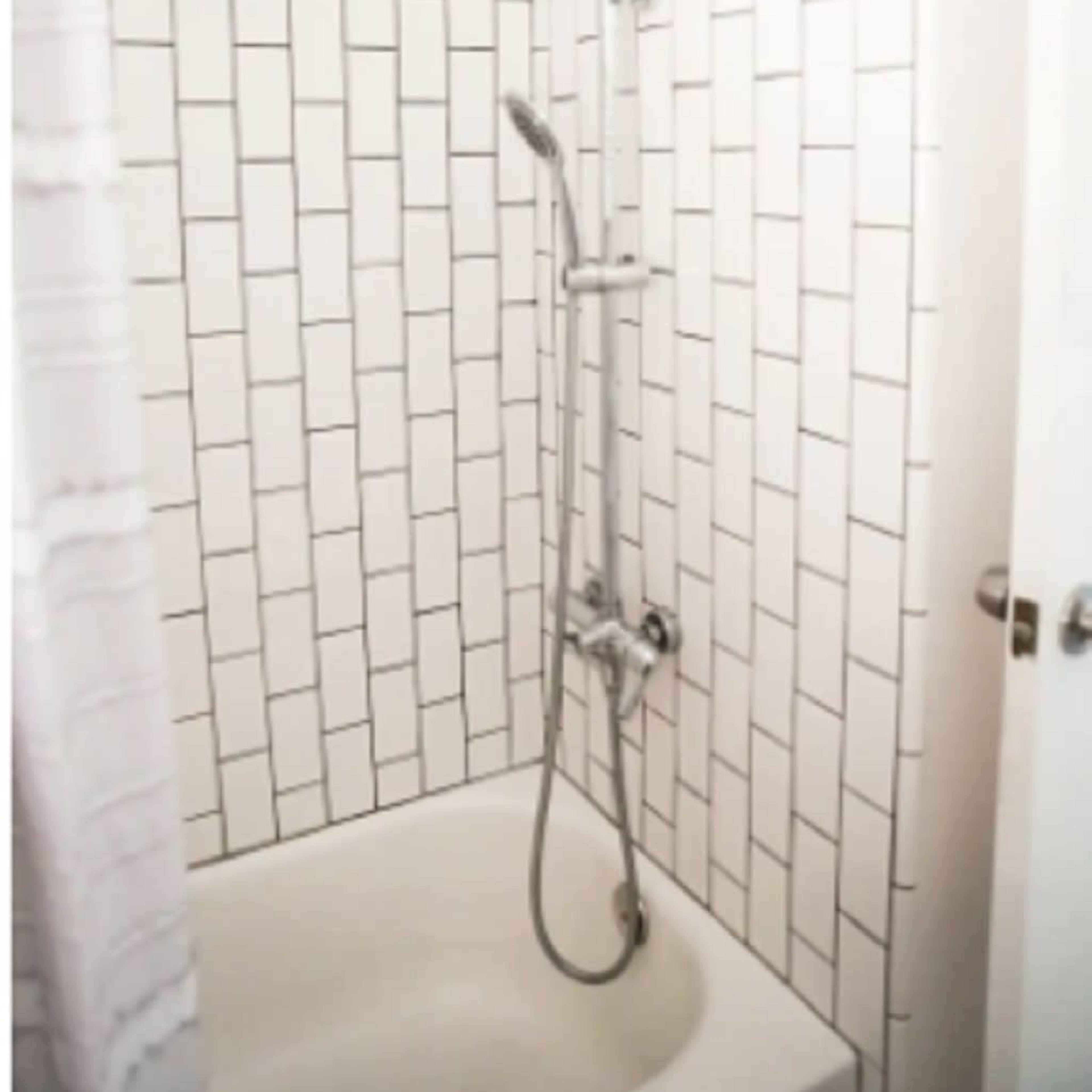 A shower area with a rainfall showerhead and a handheld shower fixture, enclosed by white tiled walls and a bathtub.