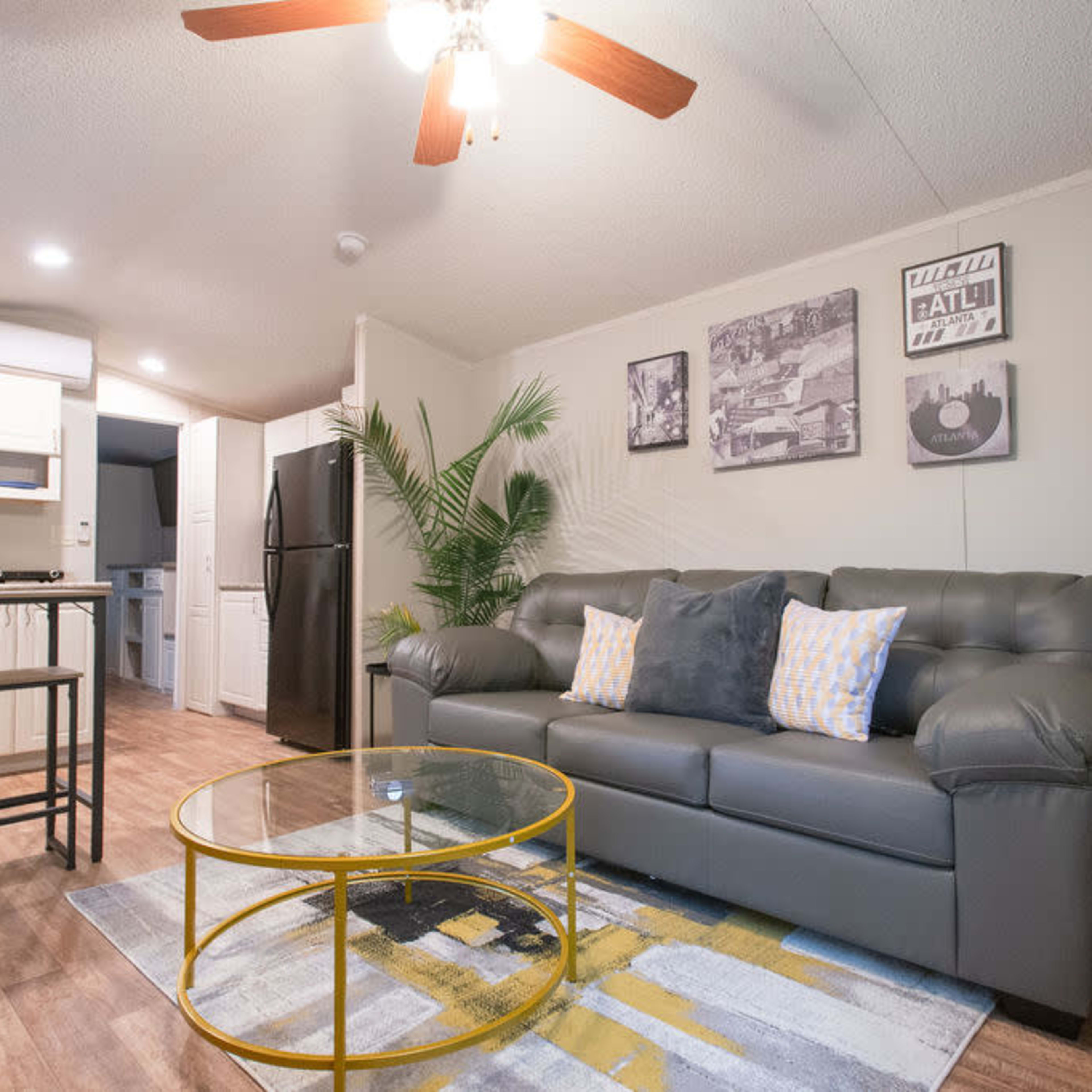 A cozy living area with a gray sofa, a round glass coffee table, and modern decor, including framed pictures on the wall and a plant in the corner.