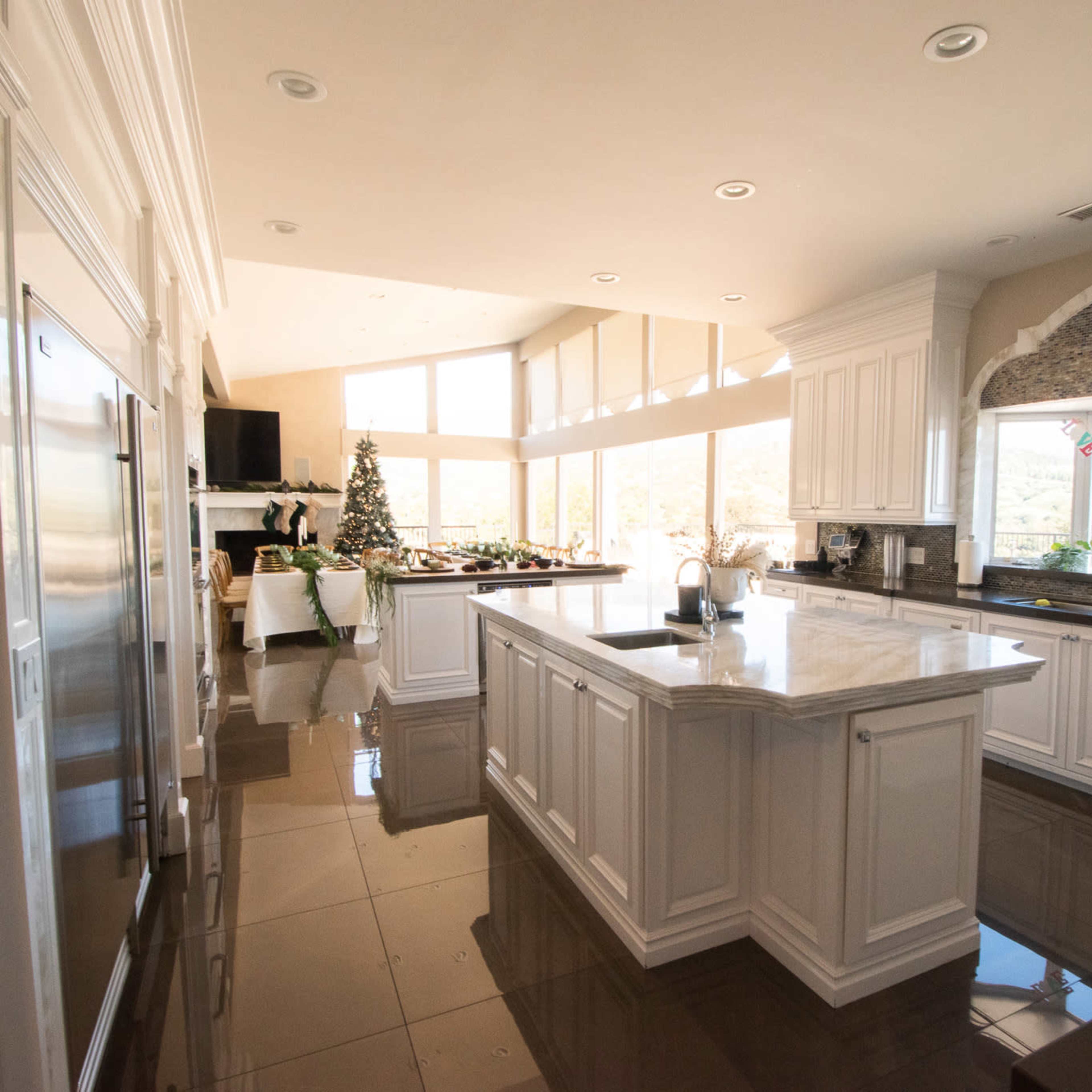 A spacious kitchen with a large island, white cabinetry, and a view of mountains through large windows.