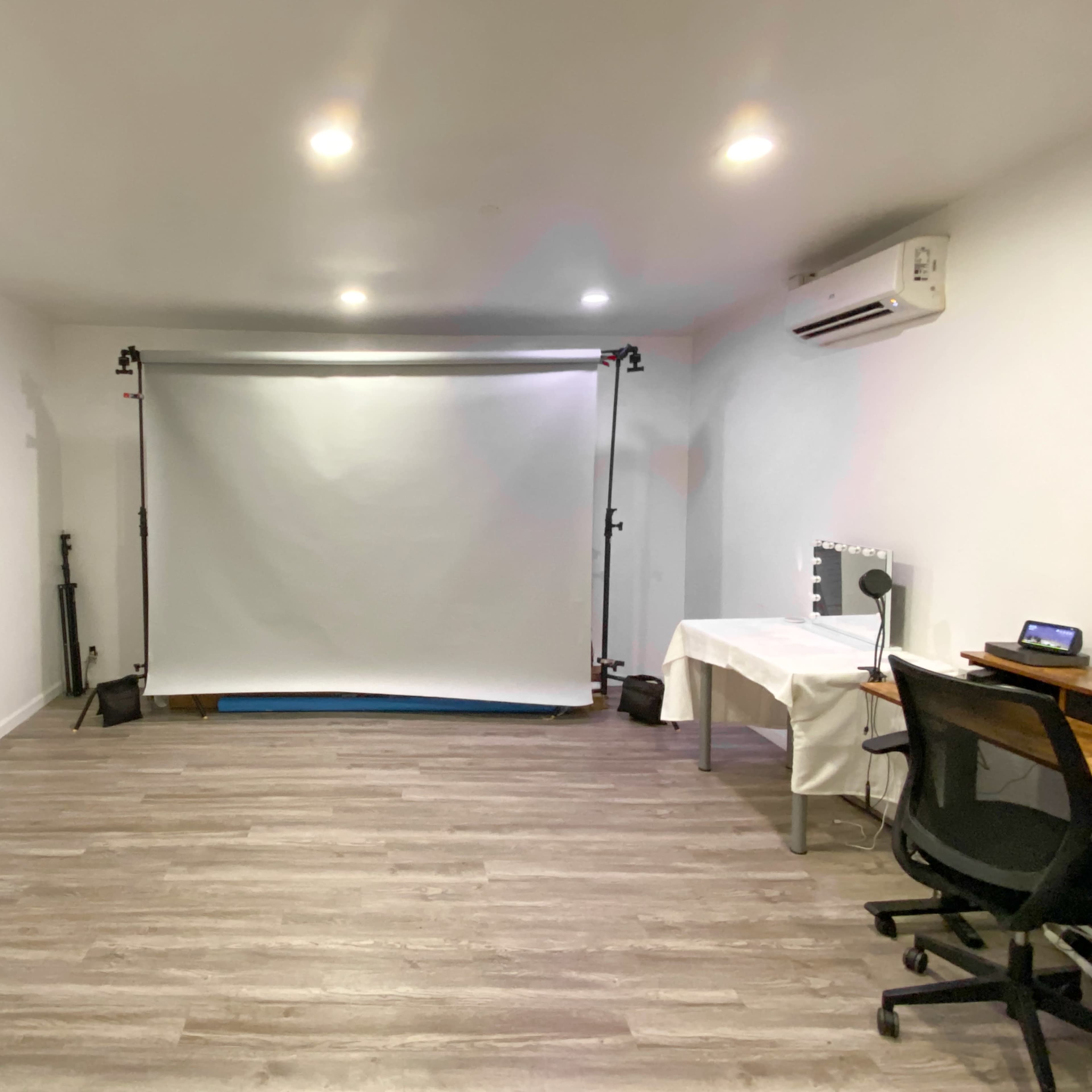 A minimalist studio space with a white backdrop, a table, a chair, and overhead lighting.