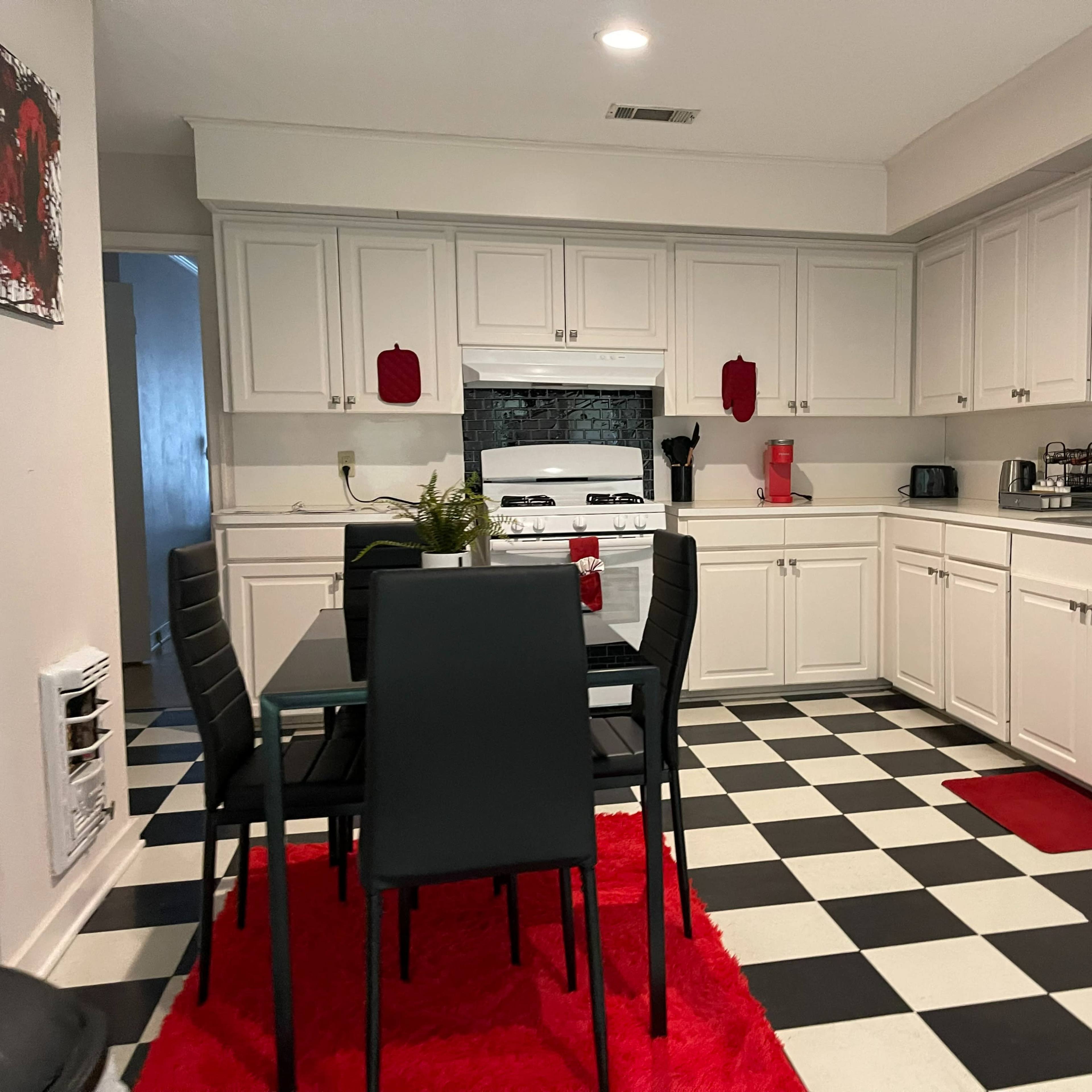 A kitchen with black and white checkered flooring, white cabinets, a dining table with black chairs, and red accents.