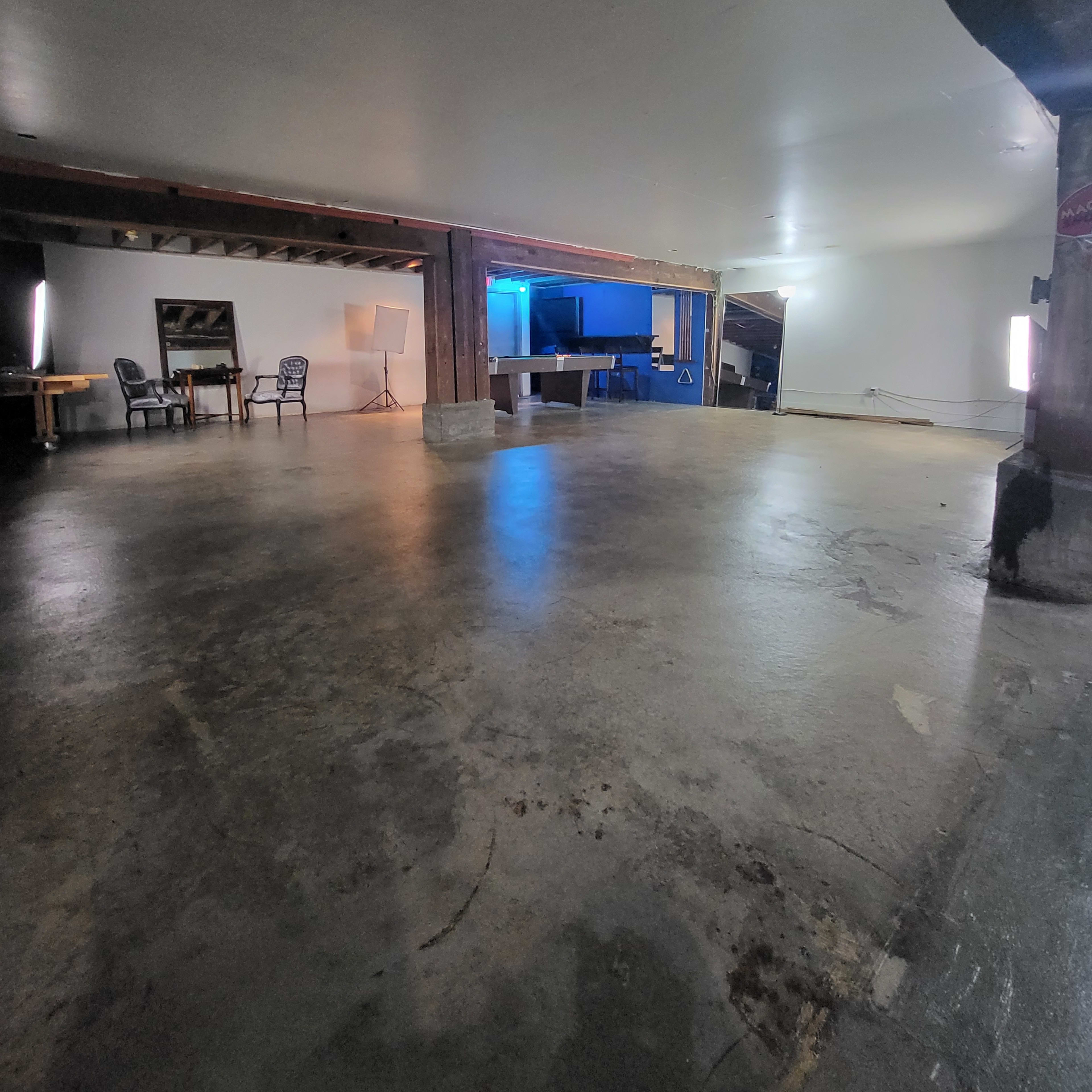 A spacious, empty room with a concrete floor, exposed beams, and minimal lighting.