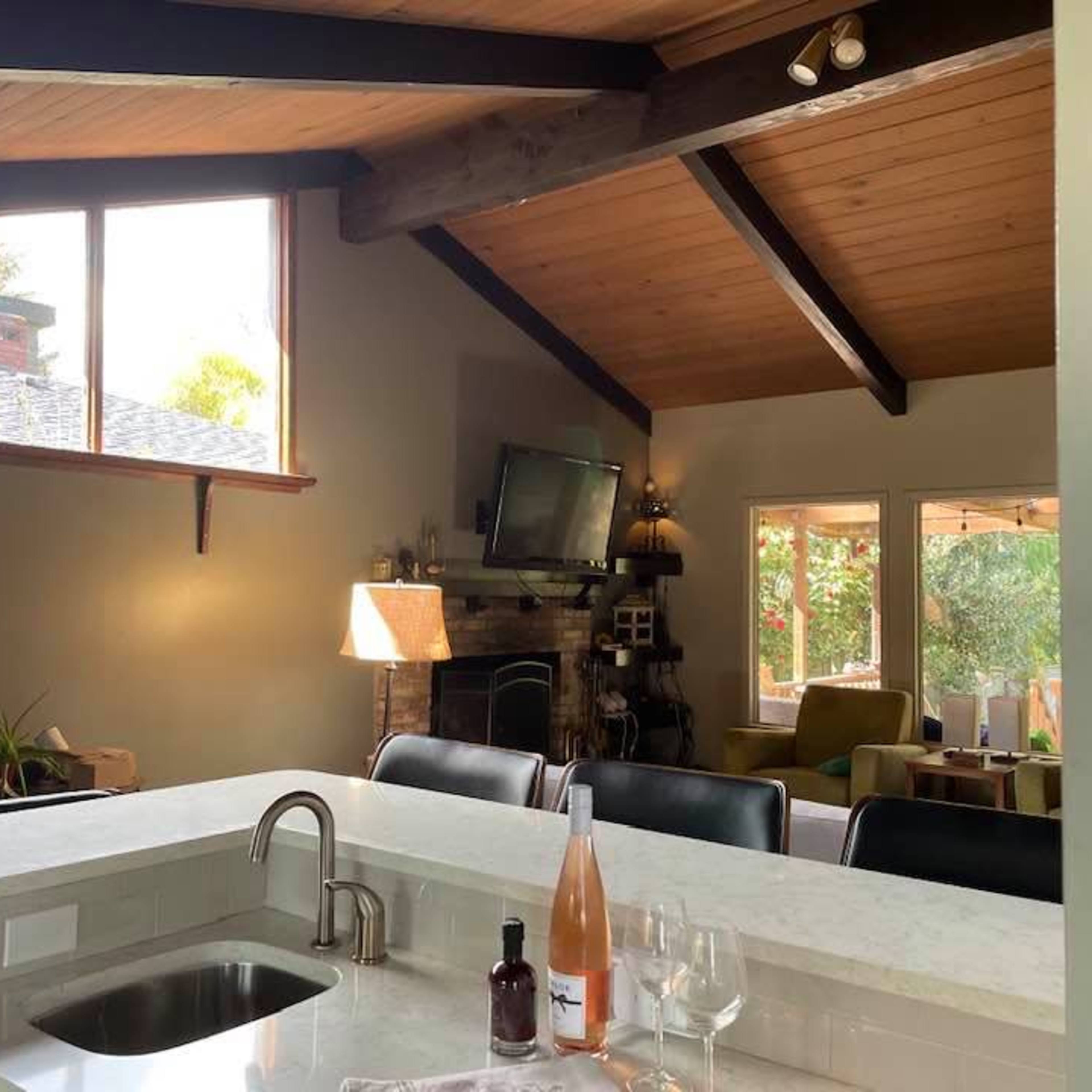 An open-concept living area with a kitchen bar, a stone fireplace, and large windows letting in natural light.