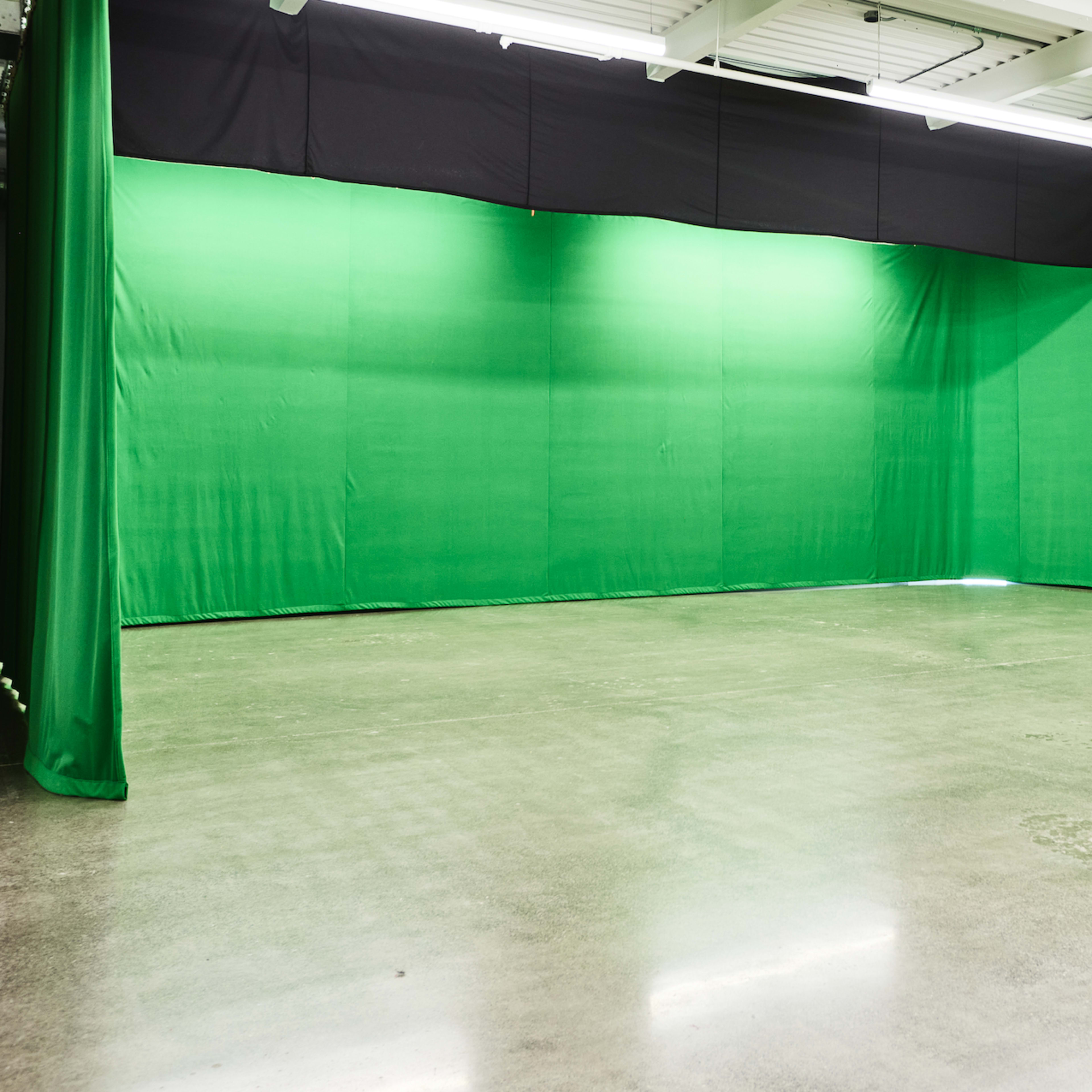 A spacious studio with green screens covering the walls and a polished concrete floor.