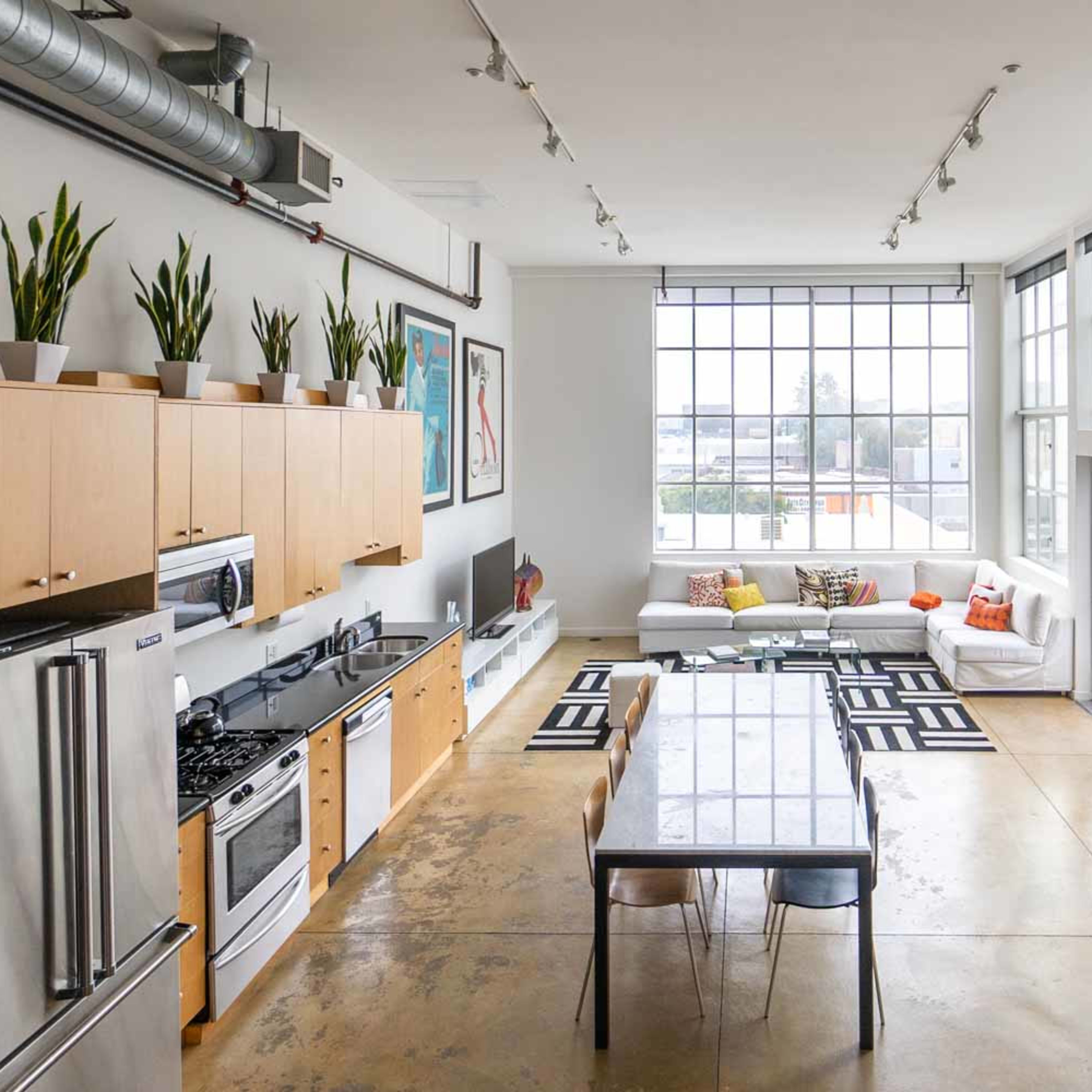 A spacious, modern kitchen and living area with large windows, a dining table, and a surfboard leaning against the wall.