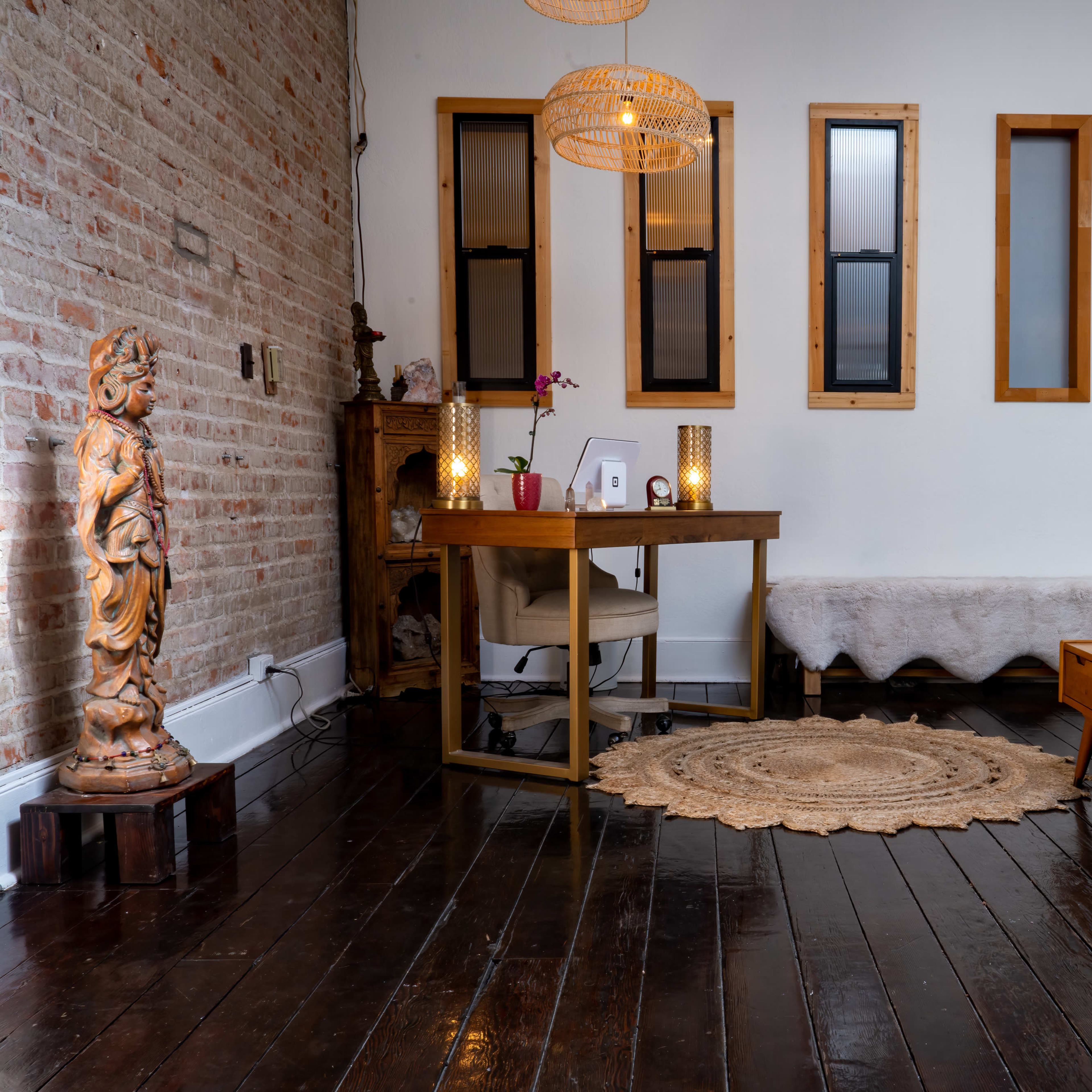 A well-decorated room featuring a desk with flowers, a plush sofa, a coffee table, and a decorative statue against a brick wall.