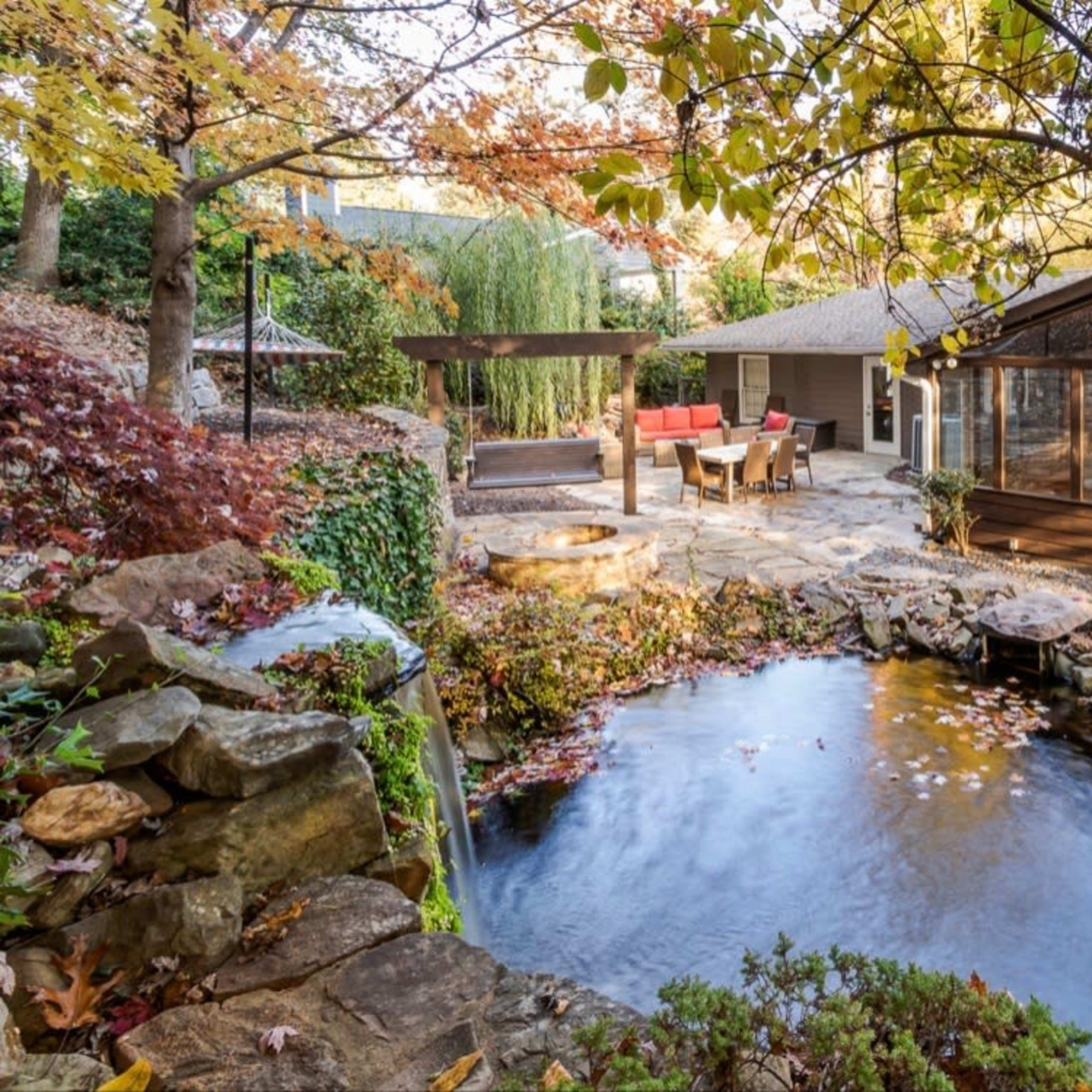 A landscaped backyard with a pond surrounded by rocks and autumn foliage, featuring a wooden deck and seated area.