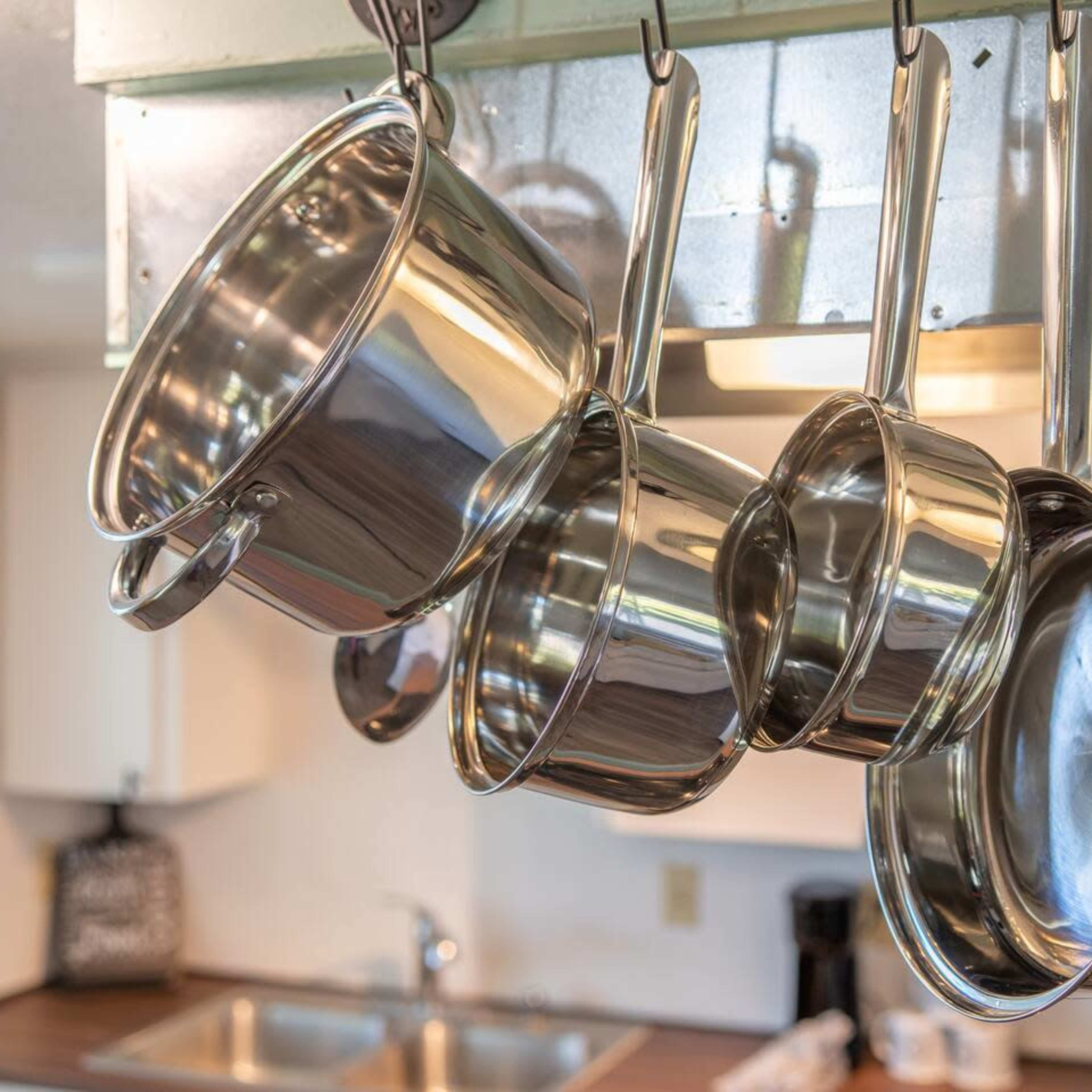 A set of stainless steel pots and pans hang from a rack in a kitchen.